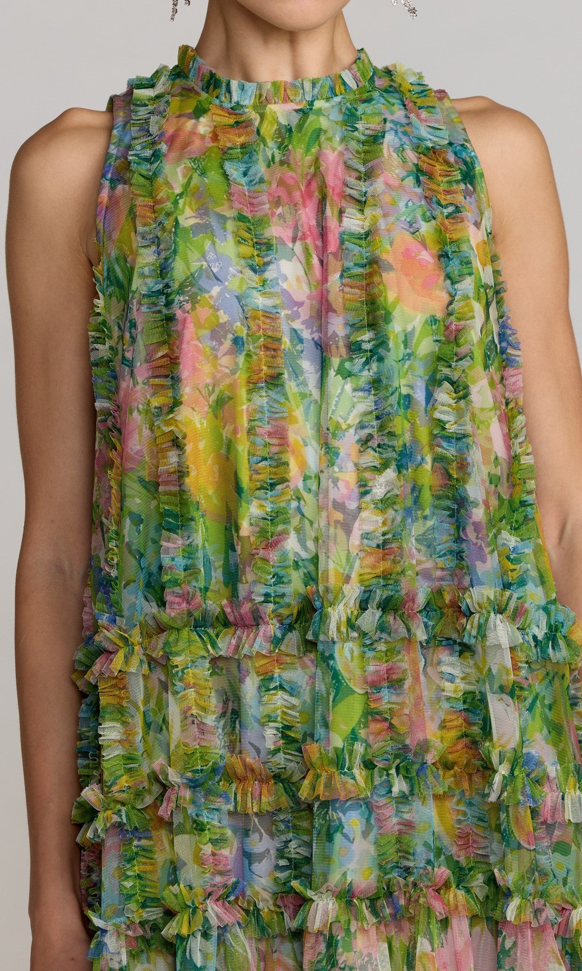 A person wearing the Mac Duggal 8488 Short Party Dress—a sleeveless mini design featuring a vibrant floral pattern and horizontal ruffled layers—shown from shoulders to mid-torso. This lively dress showcases the playful elegance distinctive of Mac Duggal creations.