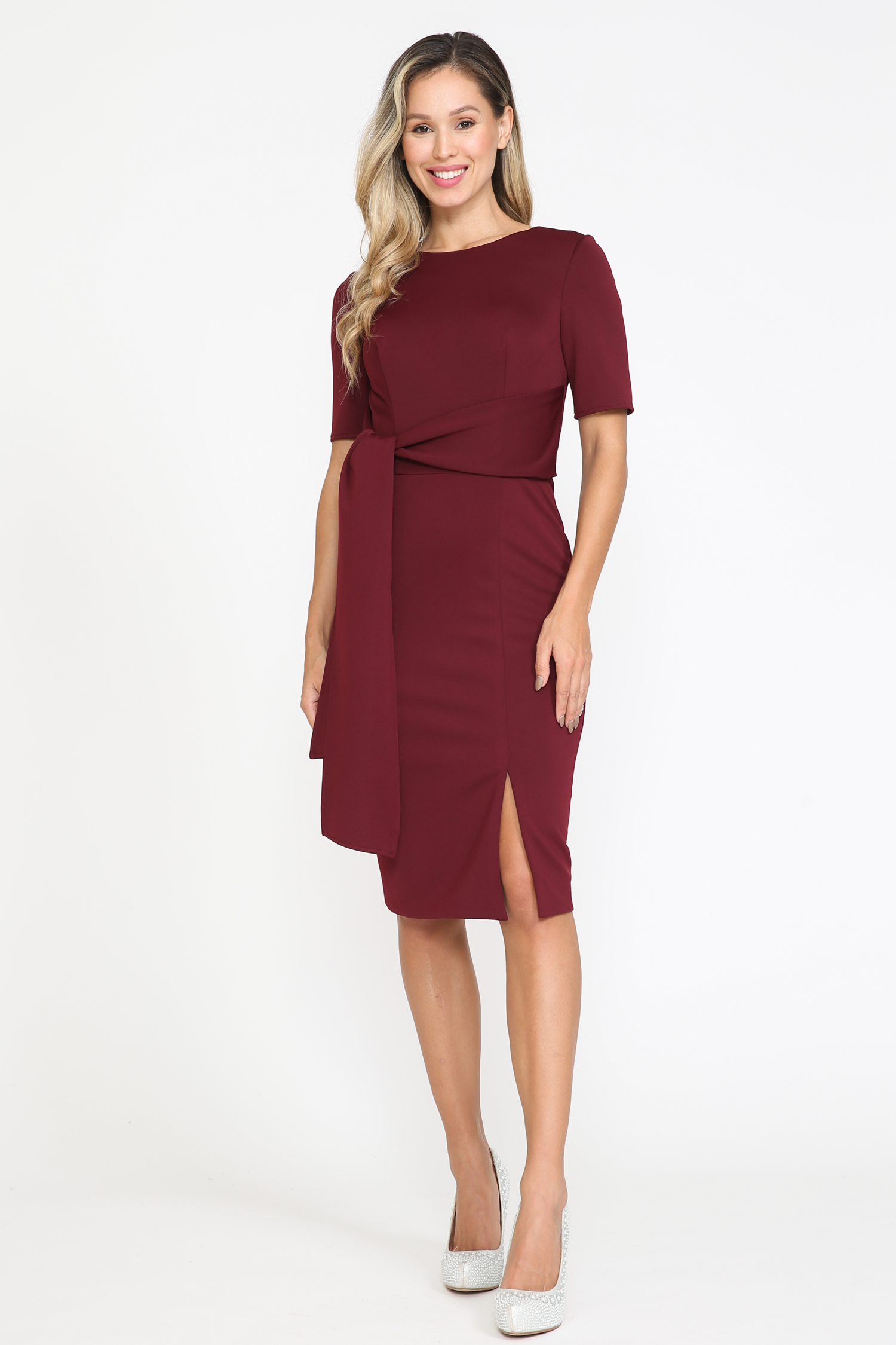 A woman stands against a white background wearing the Short Sleeve Classy Knee-Length Party Dress 8524 in maroon, featuring short sleeves, a side slit, and sash detail, paired with white high heels.