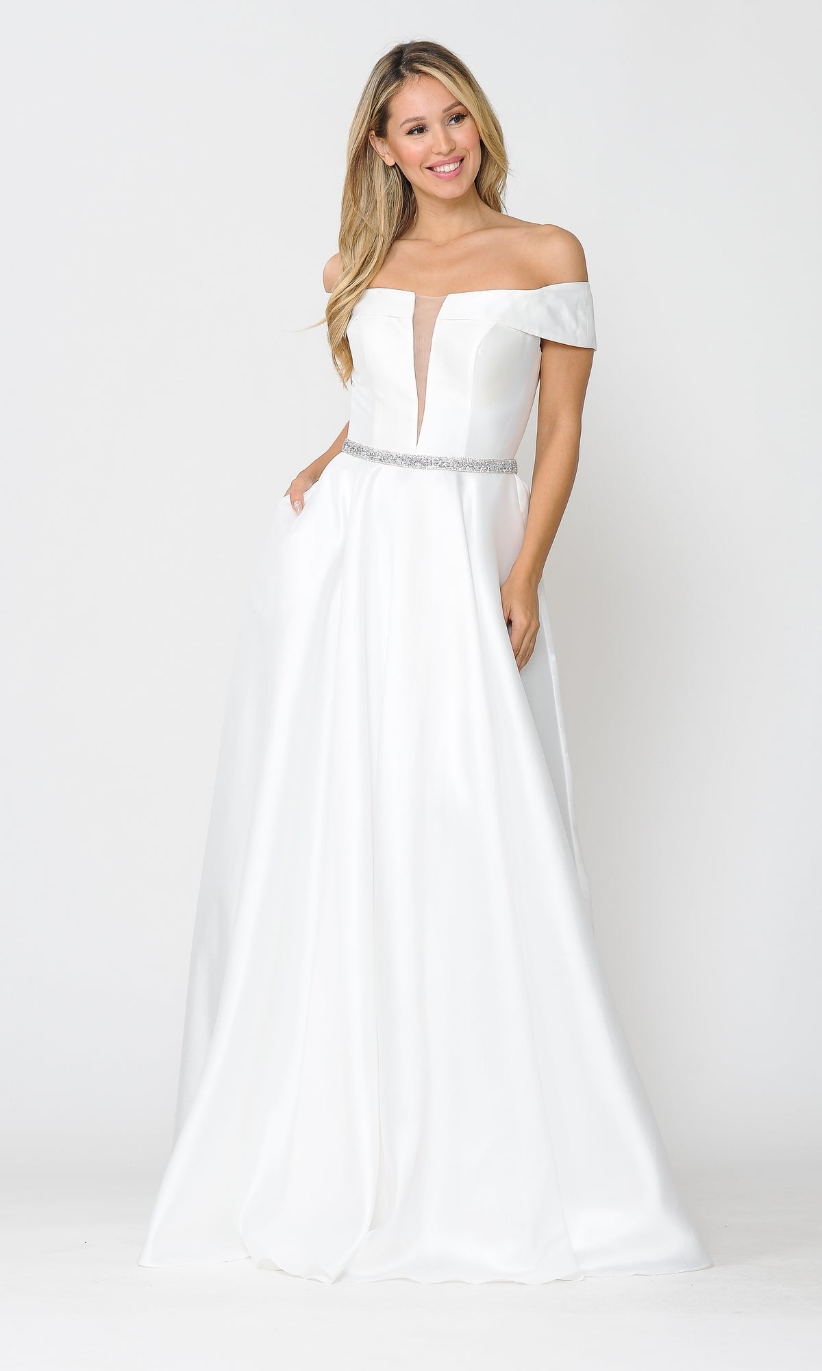 A woman smiles with her hands in her pockets, wearing the Plunging V-Neck Long Mikado Prom Ball Gown 8680—a white, floor-length off-the-shoulder dress with a deep V neckline and jeweled belt—against a plain white background.