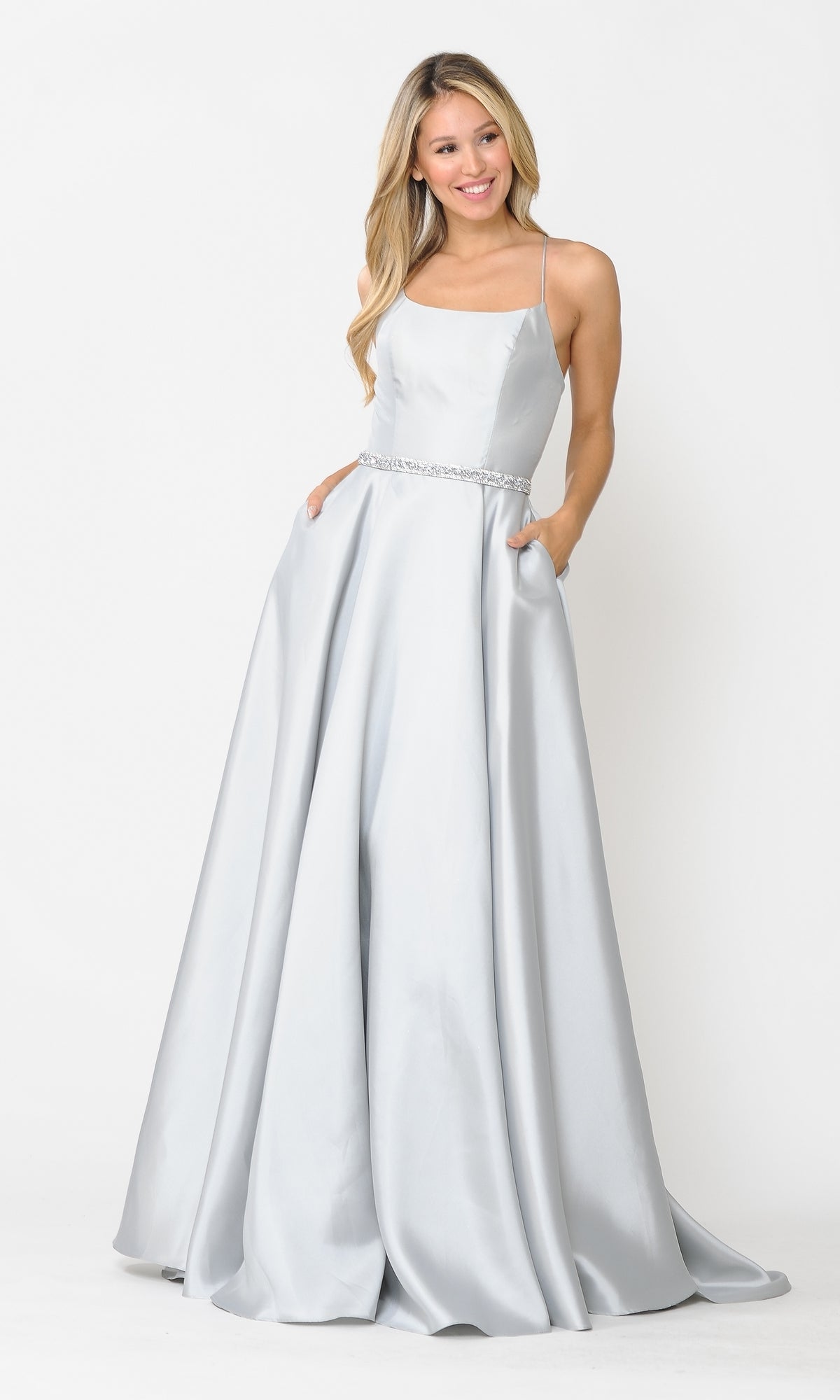 A woman stands against a white background wearing the Scoop-Neck Long A-Line Prom Dress 8684, featuring light silver satin, thin straps, a fitted bodice, jeweled waistband, and pockets.