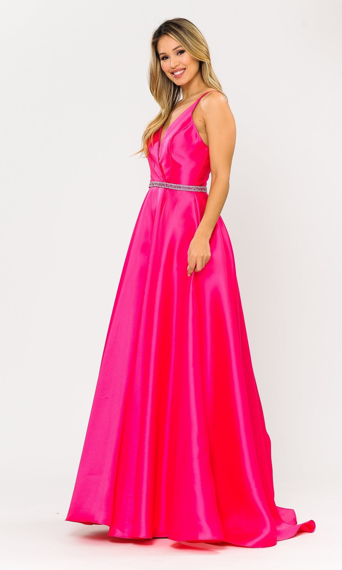 A woman in the Long A-Line Mikado Prom Gown 8690 with Pockets—sleeveless, floor-length, bright pink with a V-neckline and jeweled waistband—smiles against a white background.