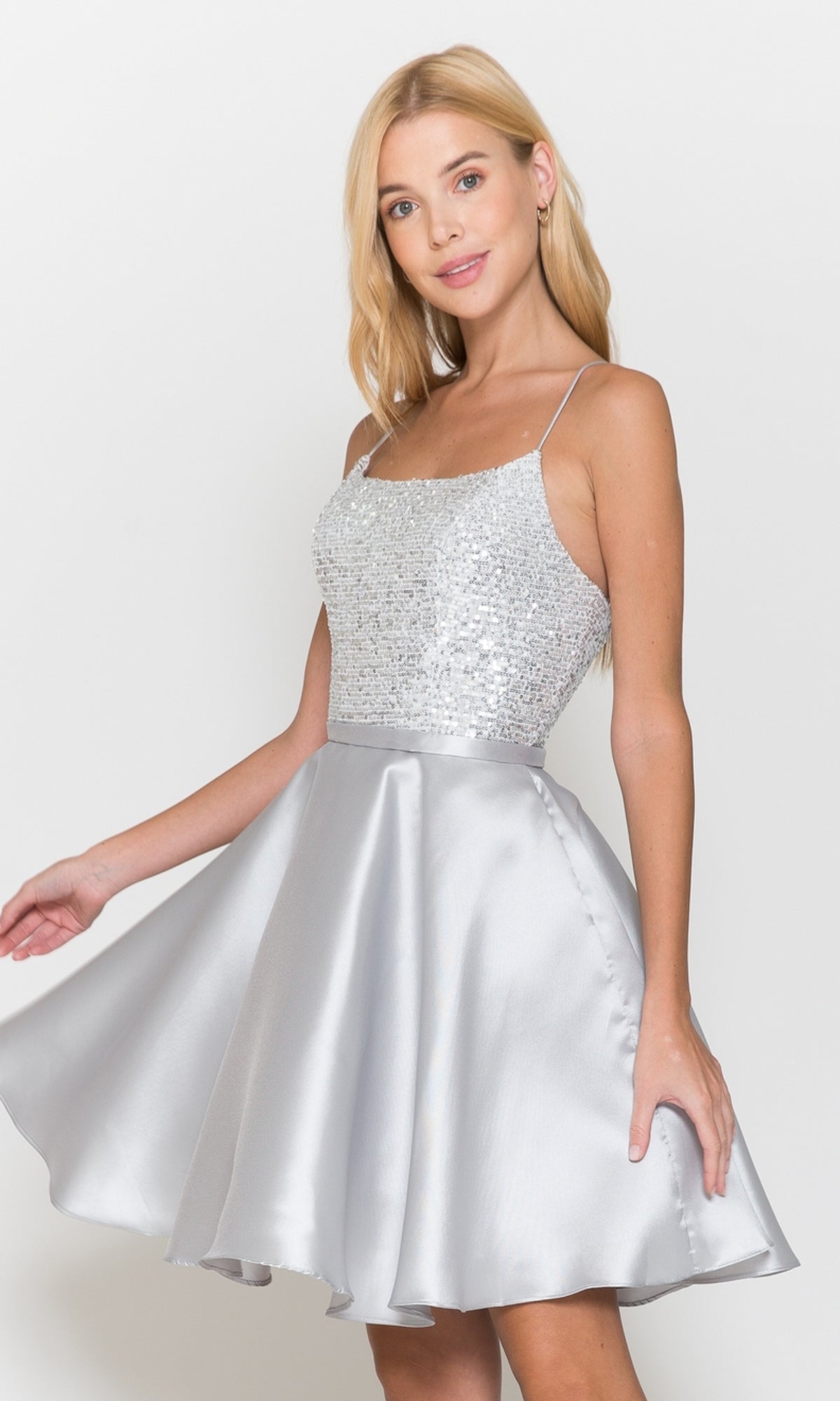 A woman stands against a plain white background wearing the Sequin-Bodice Short Flared Homecoming Dress 8730 in silver, featuring a sleeveless sequin bodice and an A-line skirt.