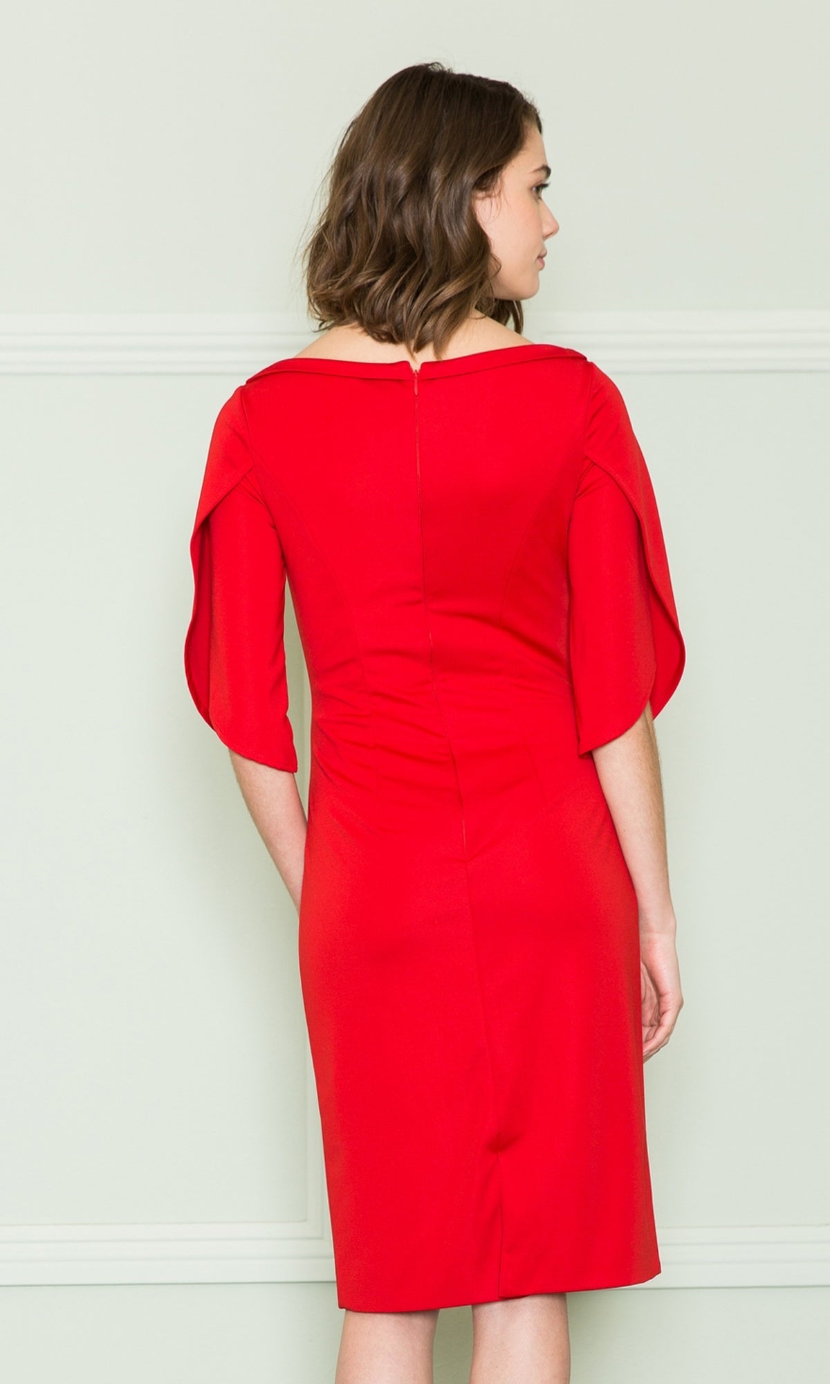 A woman faces away from the camera, modeling the Semi-formal Short Career Dress with Sleeves 8772—a bright red, knee-length sheath featuring short, loose sleeves. She stands against a light wall, highlighting this bold and sophisticated work dress.