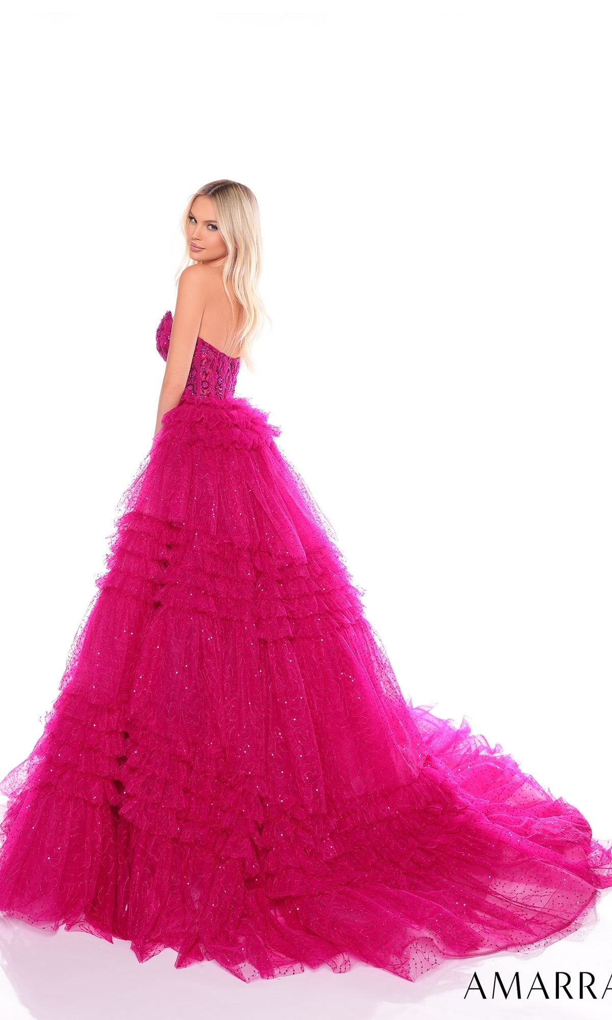 A woman wears the Long Formal Dress 88099 by Amarra, featuring a strapless sheer corset bodice, bright pink ruffled layered skirt, and a dramatic long train, standing against a white background.