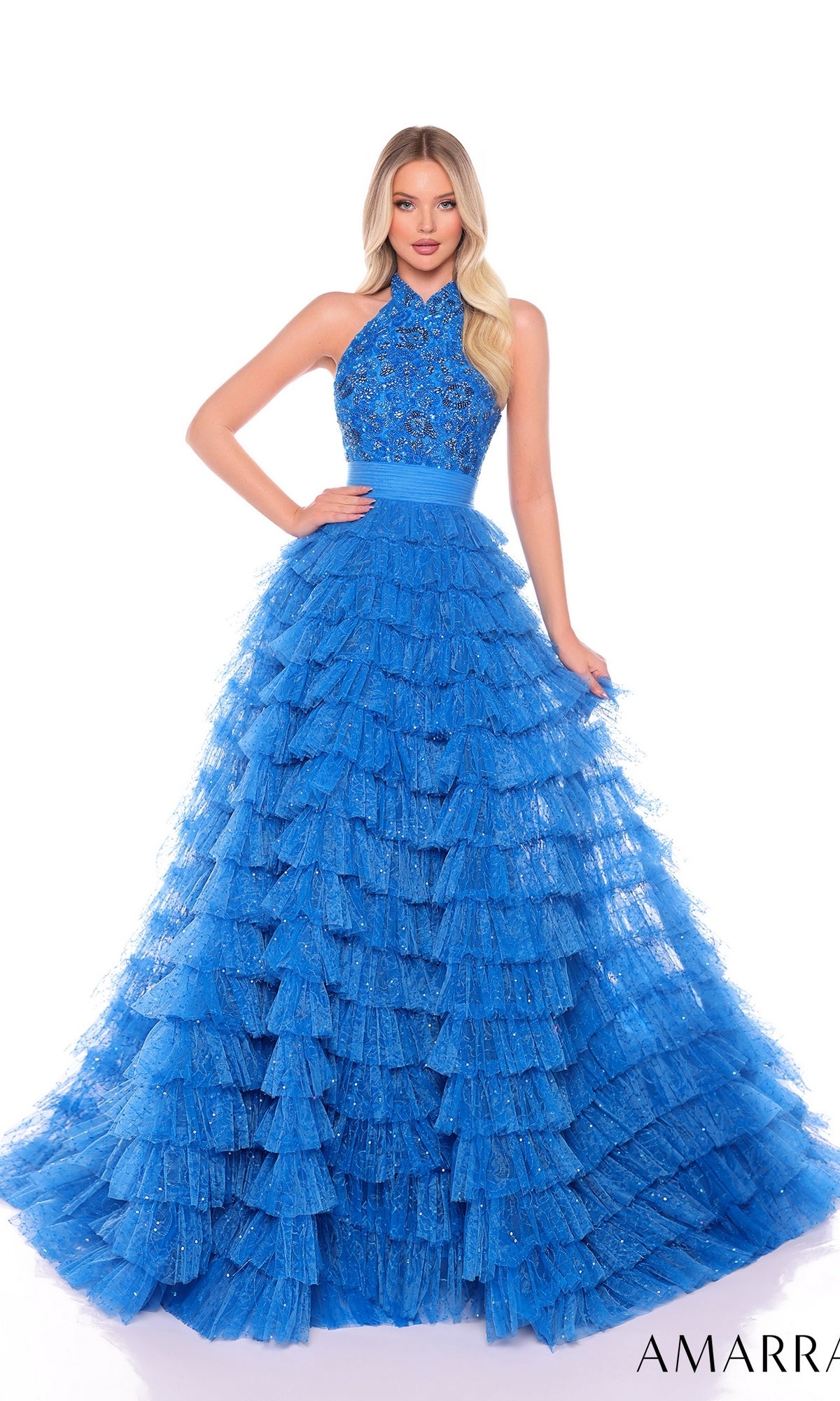 A woman wears the Long Formal Dress 88102 by Amarra, a sleeveless bright blue halter-neck ball gown with a beaded bodice and tiered ruffled skirt, standing against a white background.