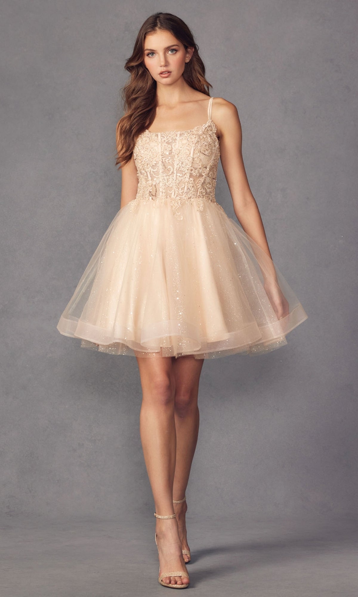 A woman stands against a gray background wearing the Sheer-Bodice Short A-Line Prom Dress 883, featuring a fitted corset-style bodice and strappy heels.