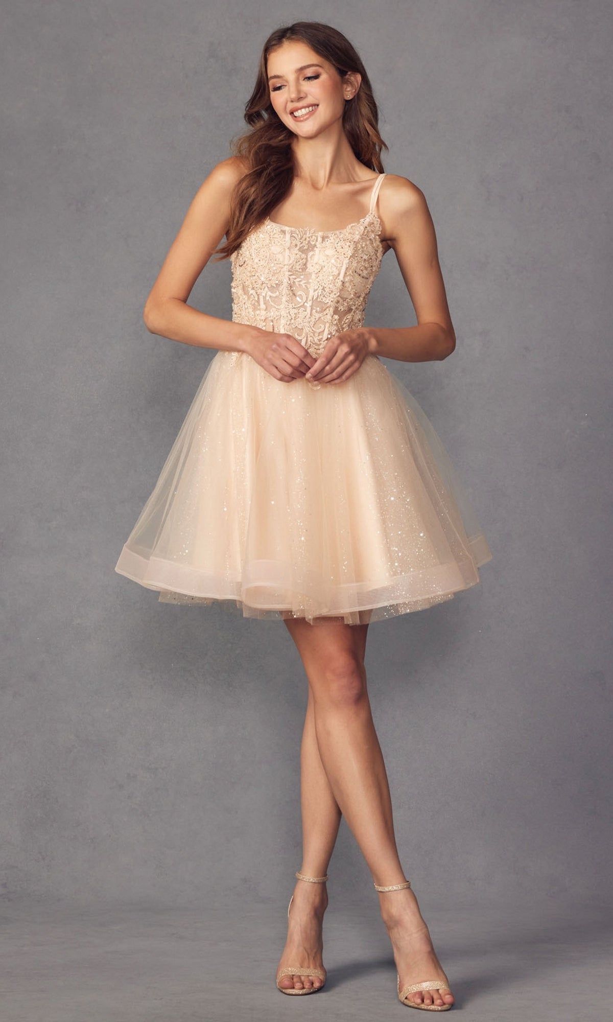 A woman wears the Sheer-Bodice Short A-Line Prom Dress 883, featuring a sleeveless, light beige design with a fitted bodice and tulle skirt, standing against a gray background.