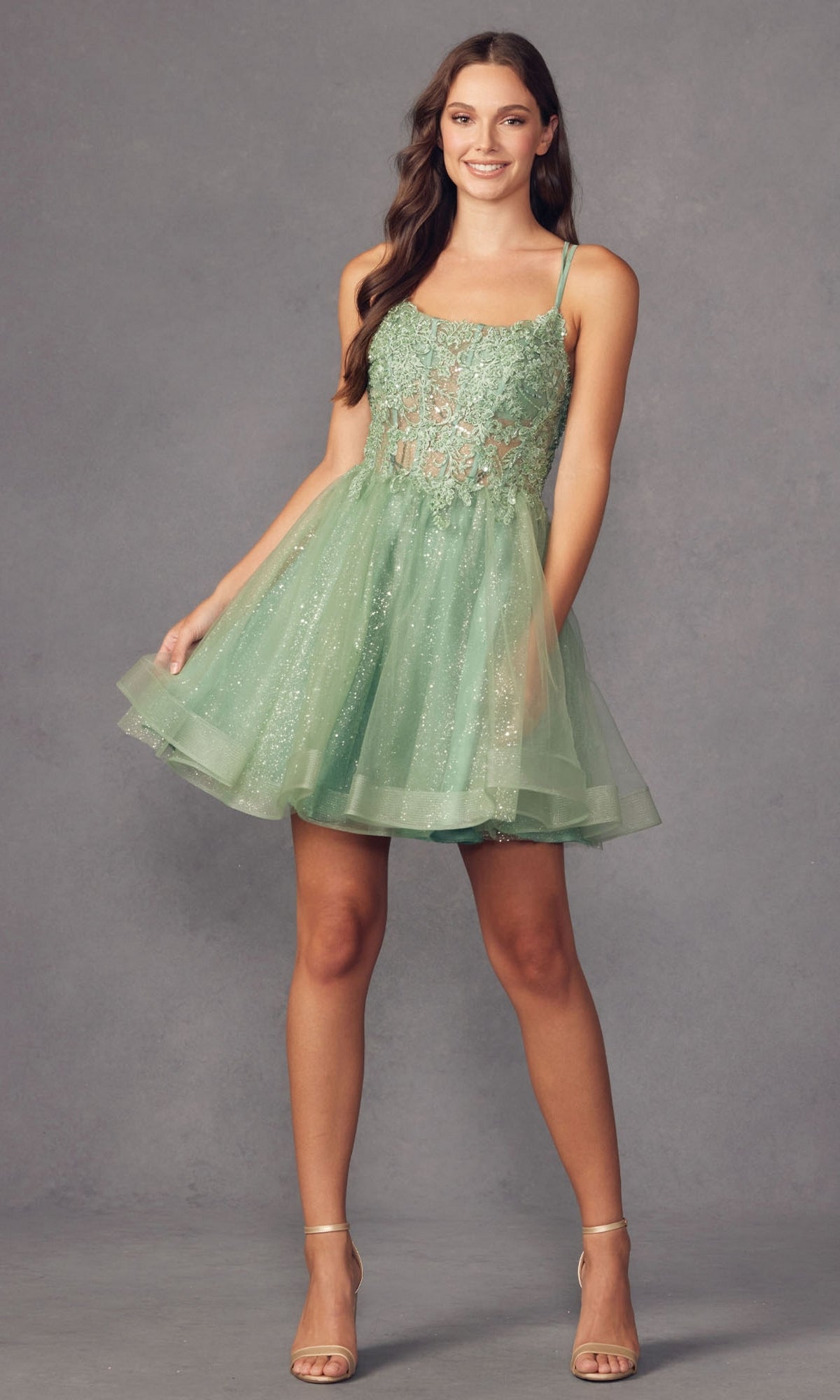 A woman poses elegantly against a gray background wearing the Sheer-Bodice Short A-Line Prom Dress 883 in light green, featuring a sheer lace corset-style bodice, layered tulle skirt, and nude heels.