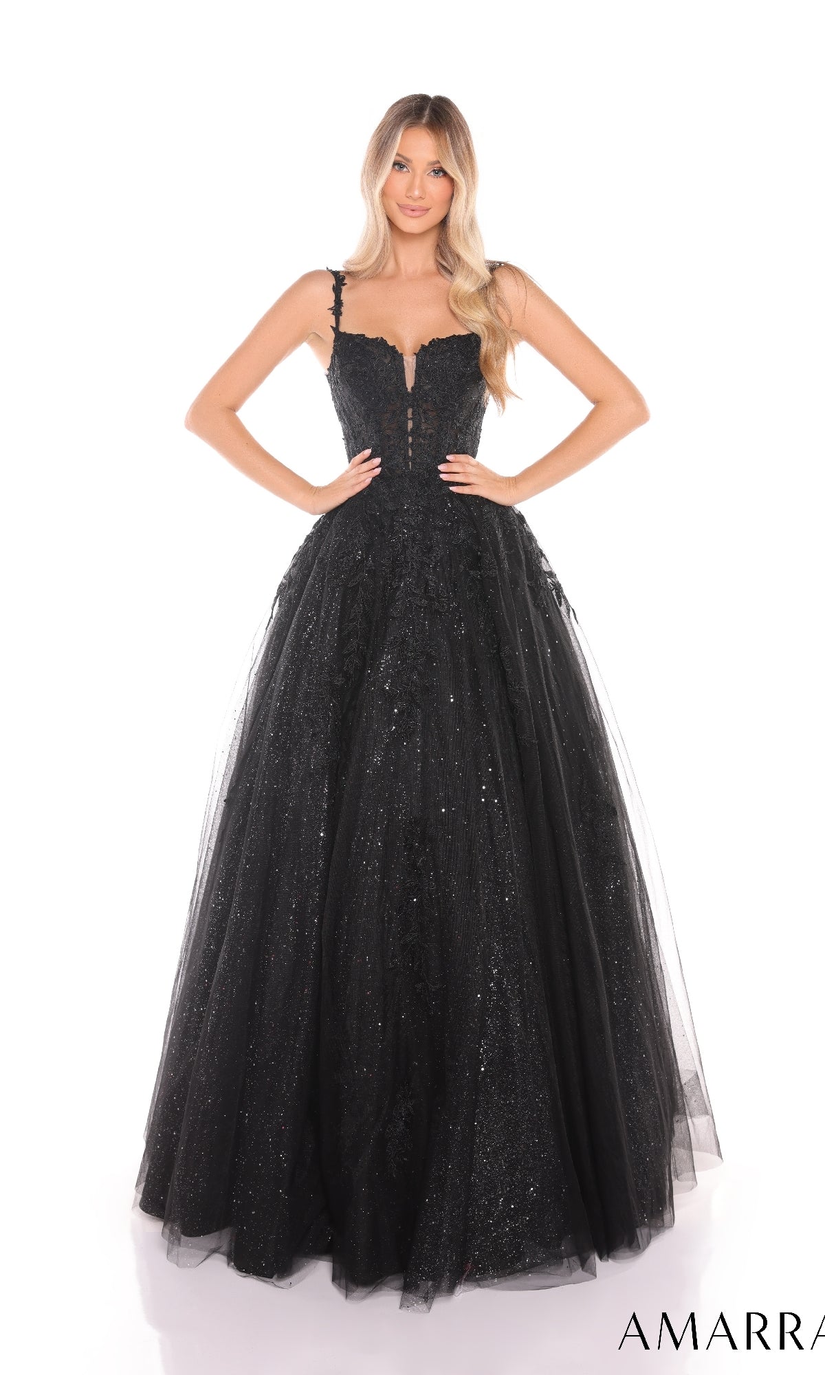 A woman in the Amarra 88590 Floral Lace Prom Ball Gown, featuring black sparkly glitter tulle, thin straps, and a lace-up back, stands with hands on hips against a white background.