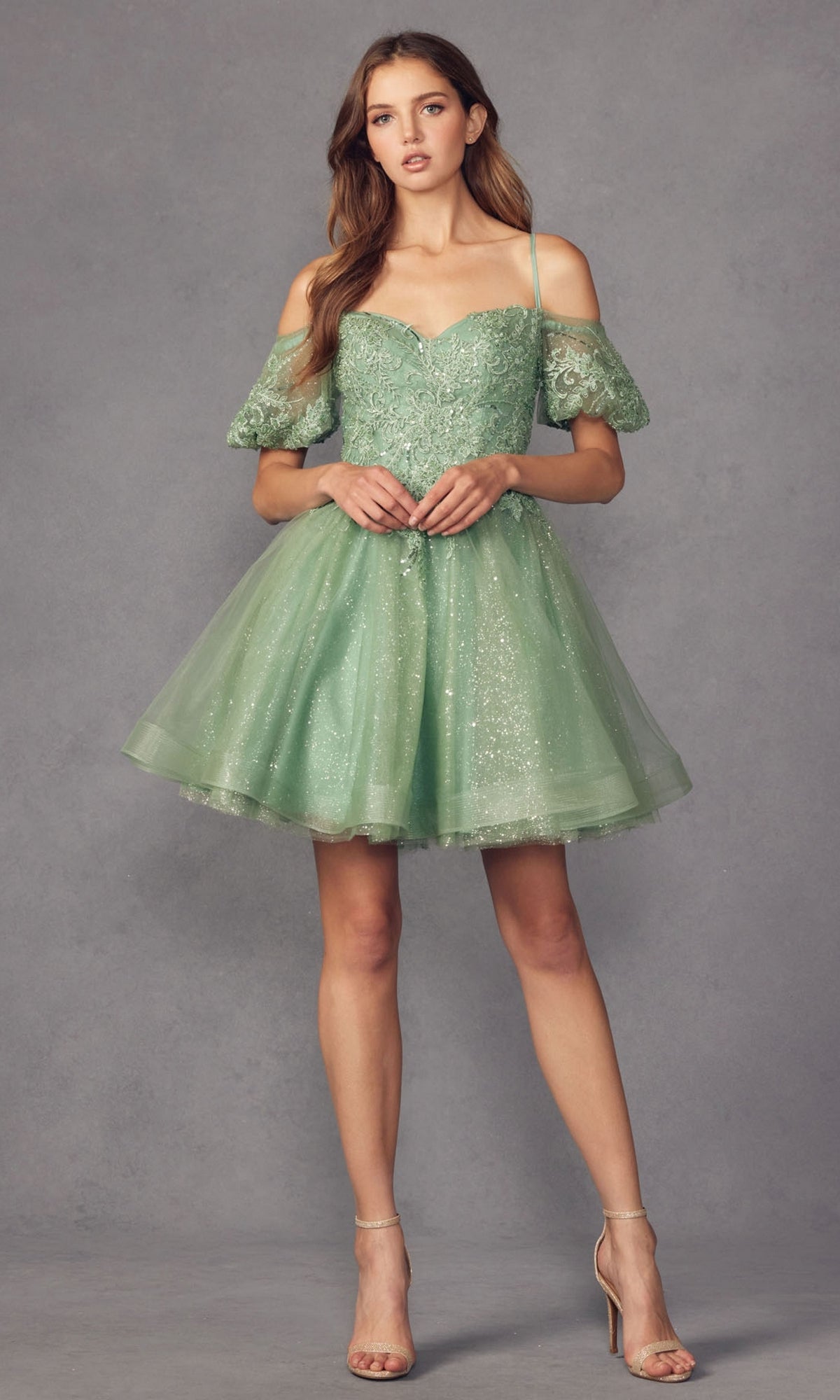 A woman wears the Puff-Sleeve Short A-Line Shimmer Prom Dress 886 in light green with lace and glitter details, cold-shoulder style, paired with nude high-heeled sandals, standing against a plain gray background.