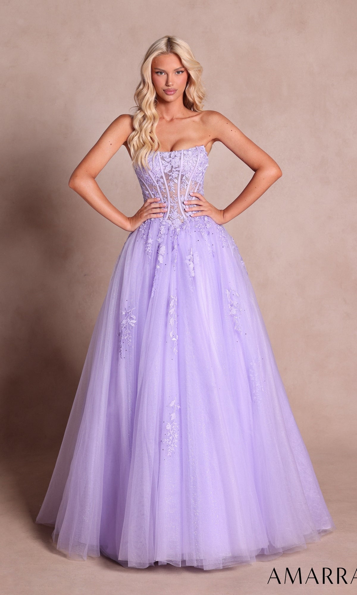 A woman wearing the Strapless Long Prom Ball Gown: Amarra 88913 in lilac—an elegant long ball gown adorned with floral embellishments and featuring a sheer lace corset bodice—stands gracefully against a beige background.