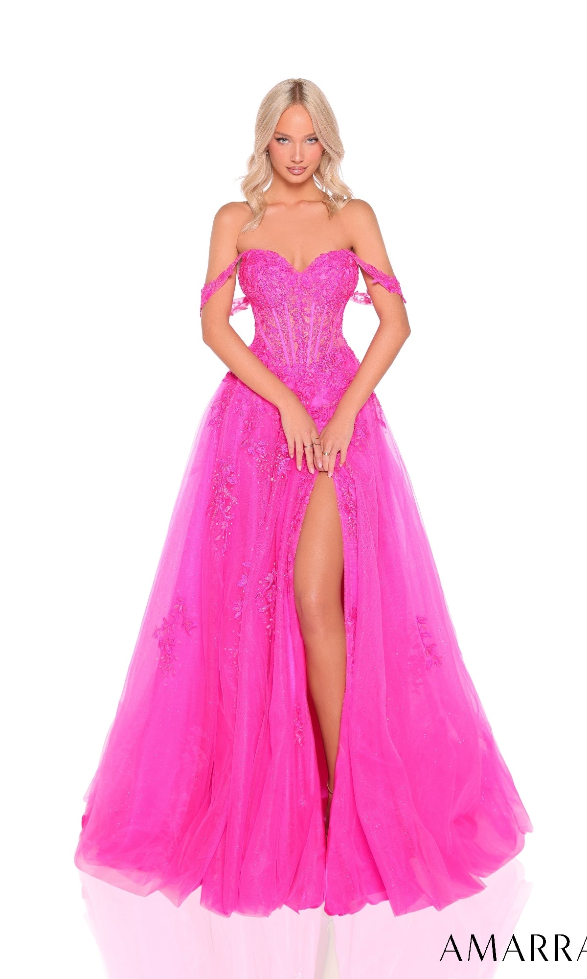 Woman wearing Amarra 88963, an off-the-shoulder corset prom ball gown in bright pink with floral embellishments, a sheer bodice, and thigh-high slit, stands against a white background.