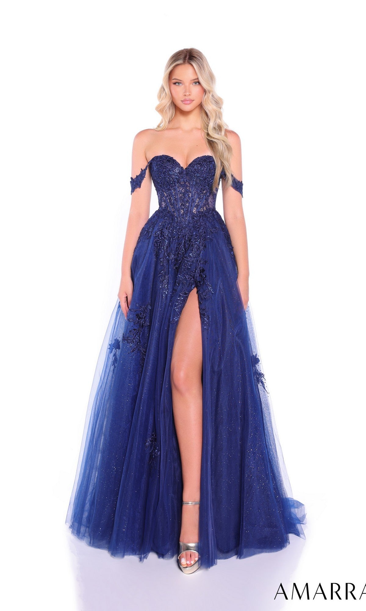 A woman in the Amarra 88963 Off-Shoulder Corset Prom Ball Gown, featuring a deep blue hue, high slit, floral appliqué, sheer corset bodice, and tulle overlay stands against a white background.