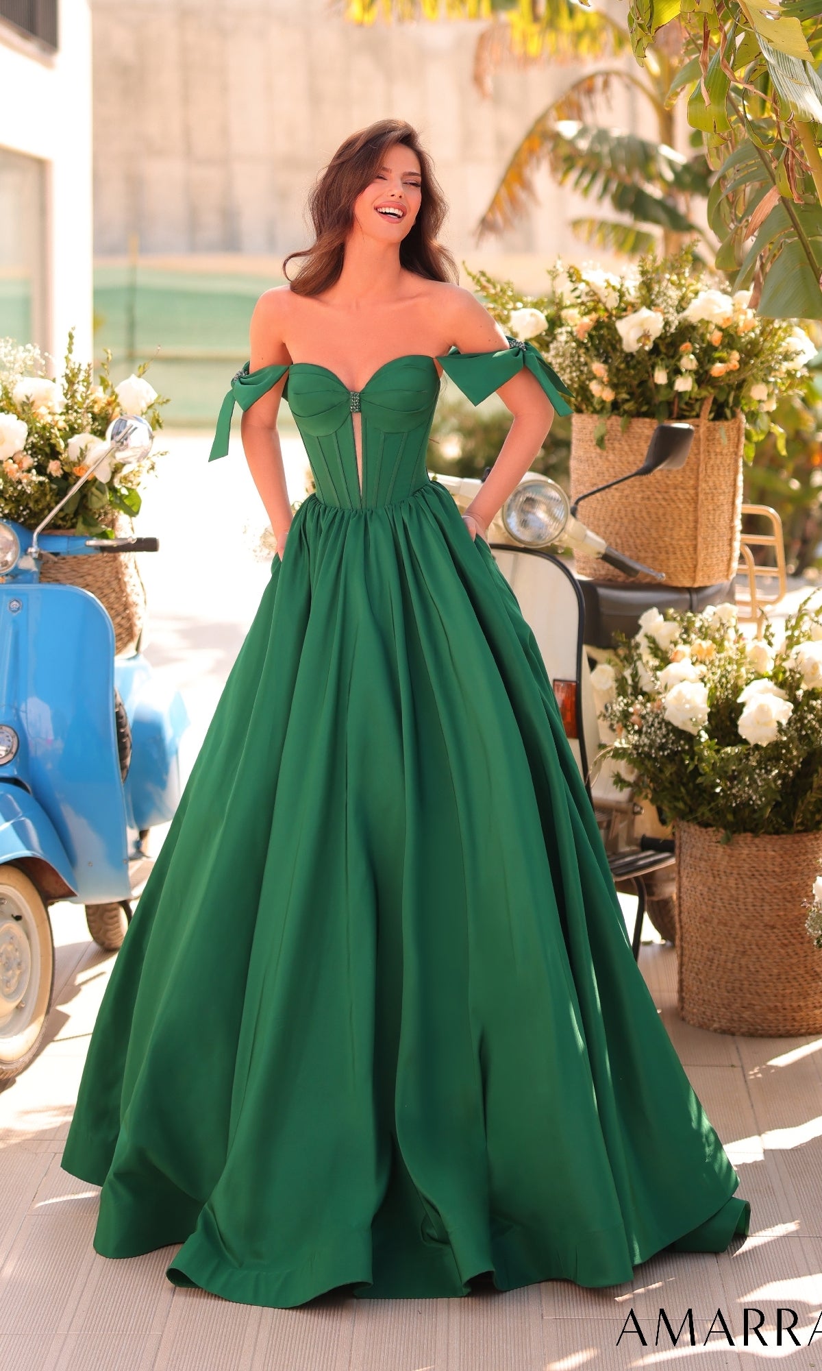 A woman in the Amarra 88995 Lace-Up Off-Shoulder Prom Ball Gown stands outside, surrounded by white flowers and a blue scooter.