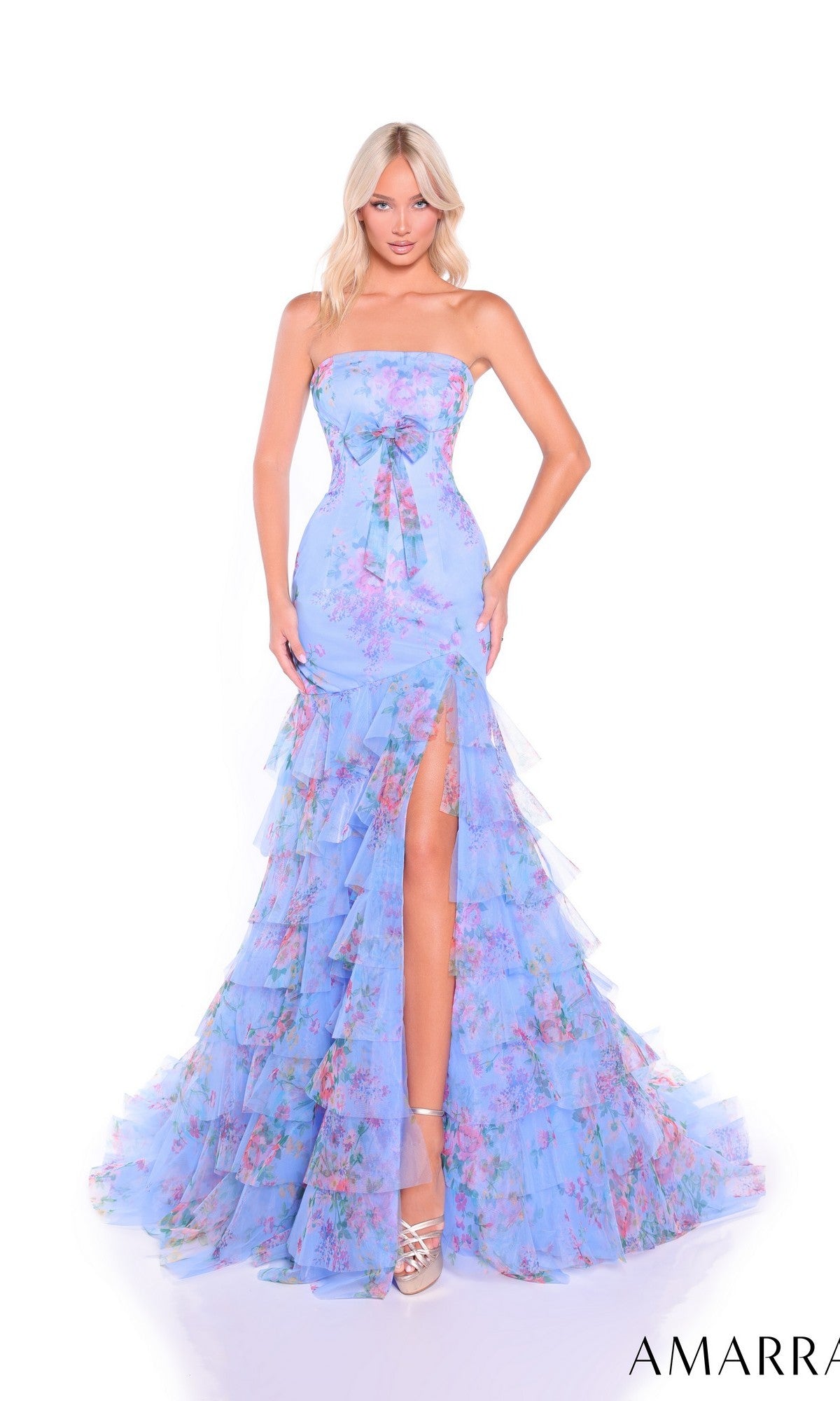 A woman models the Amarra 89075 long prom dress, which features a strapless fitted bodice and a light blue floral chiffon tiered skirt with ruffled layers and a high slit, against a white background.