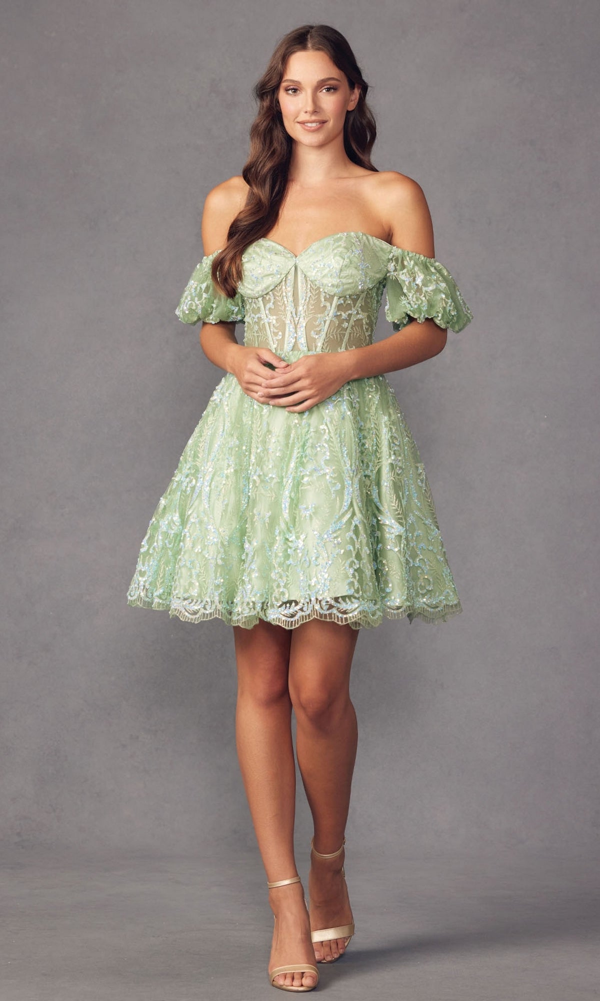 A woman stands against a plain gray background wearing the Off-Shoulder Sheer-Corset Short Prom Dress 891 in light green lace with floral patterns, sheer panels, and a corset-style waist, paired with nude high-heeled sandals.
