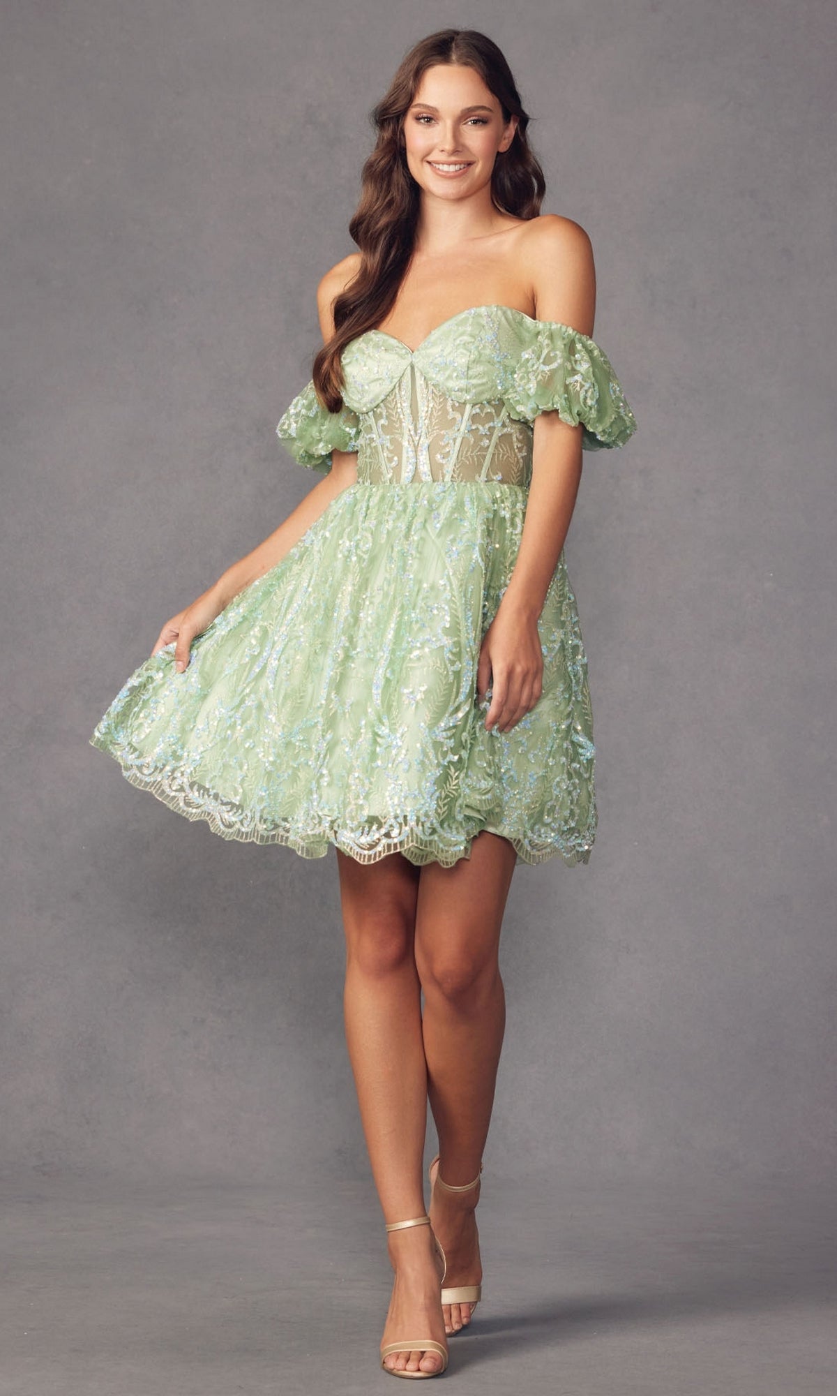 A woman wears the Off-Shoulder Sheer-Corset Short Prom Dress 891 in light green lace with puffy sleeves and nude heels, standing against a plain gray background.
