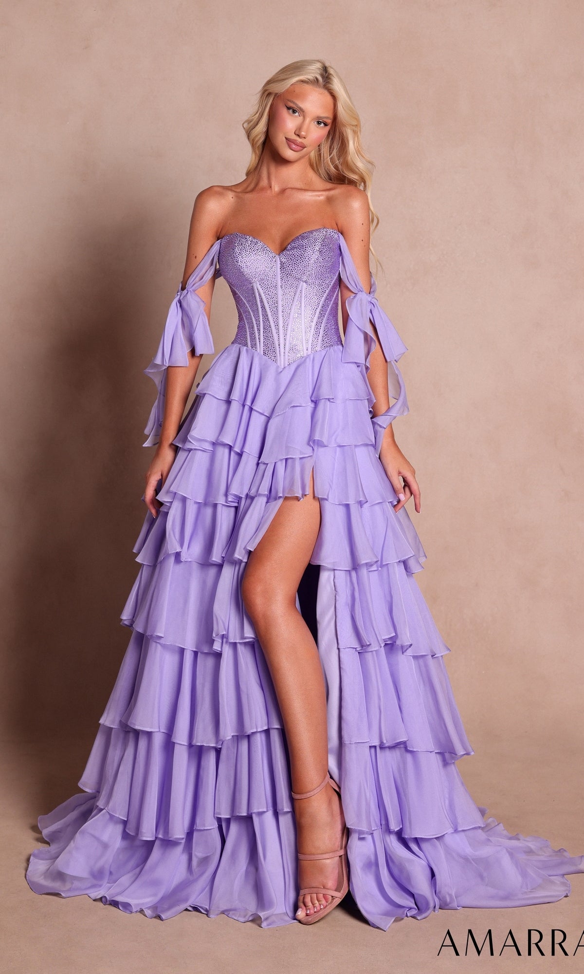 A woman wearing the Amarra 89285 long prom dress in lilac, featuring an embellished corset bodice and a high slit, stands against a plain beige background.