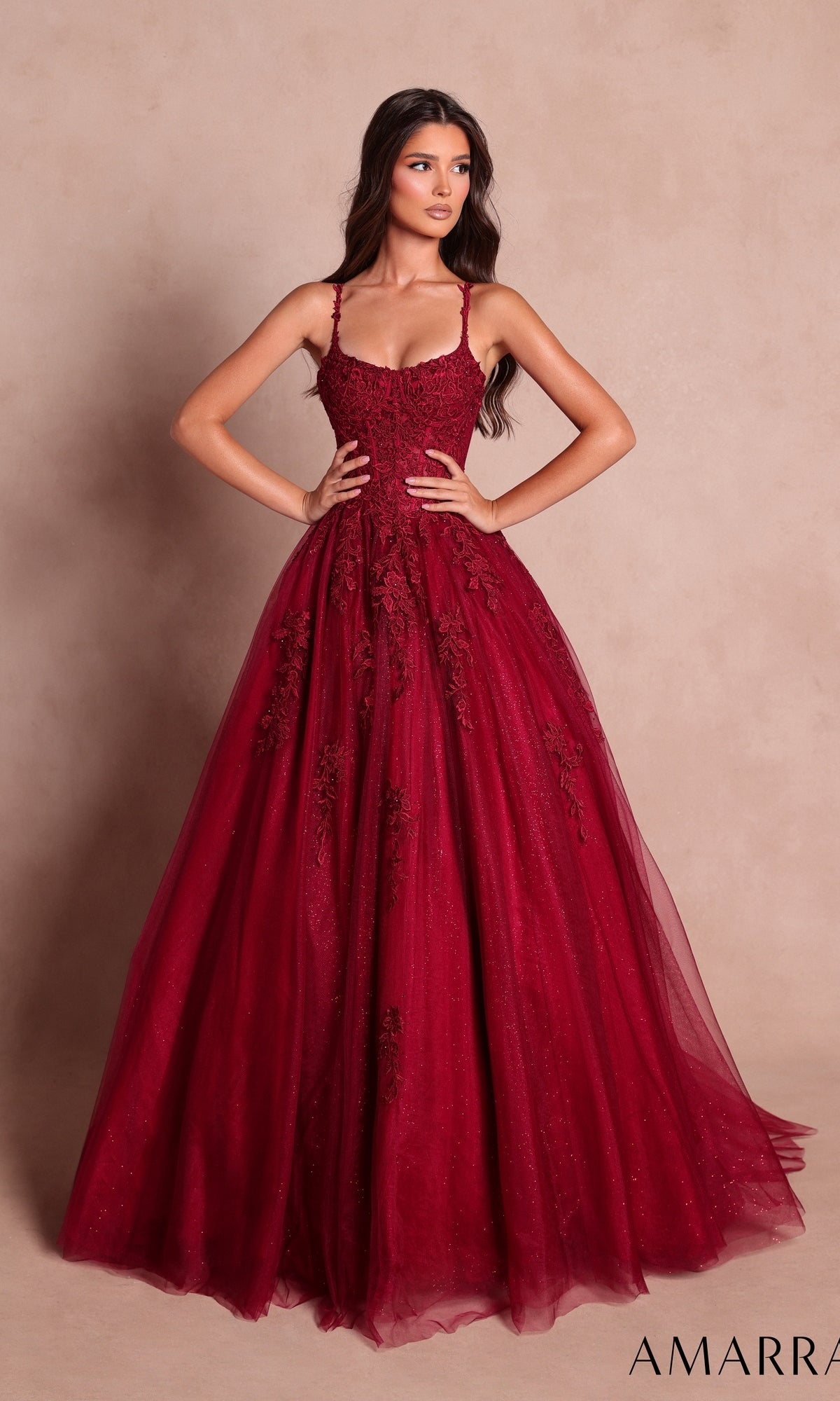 A woman wearing the Long Prom Dress: Amarra 89644 in wine—a floor-length, sleeveless gown featuring a sweetheart neckline and delicate floral lace appliqués on the fitted bodice—stands against a plain beige background.