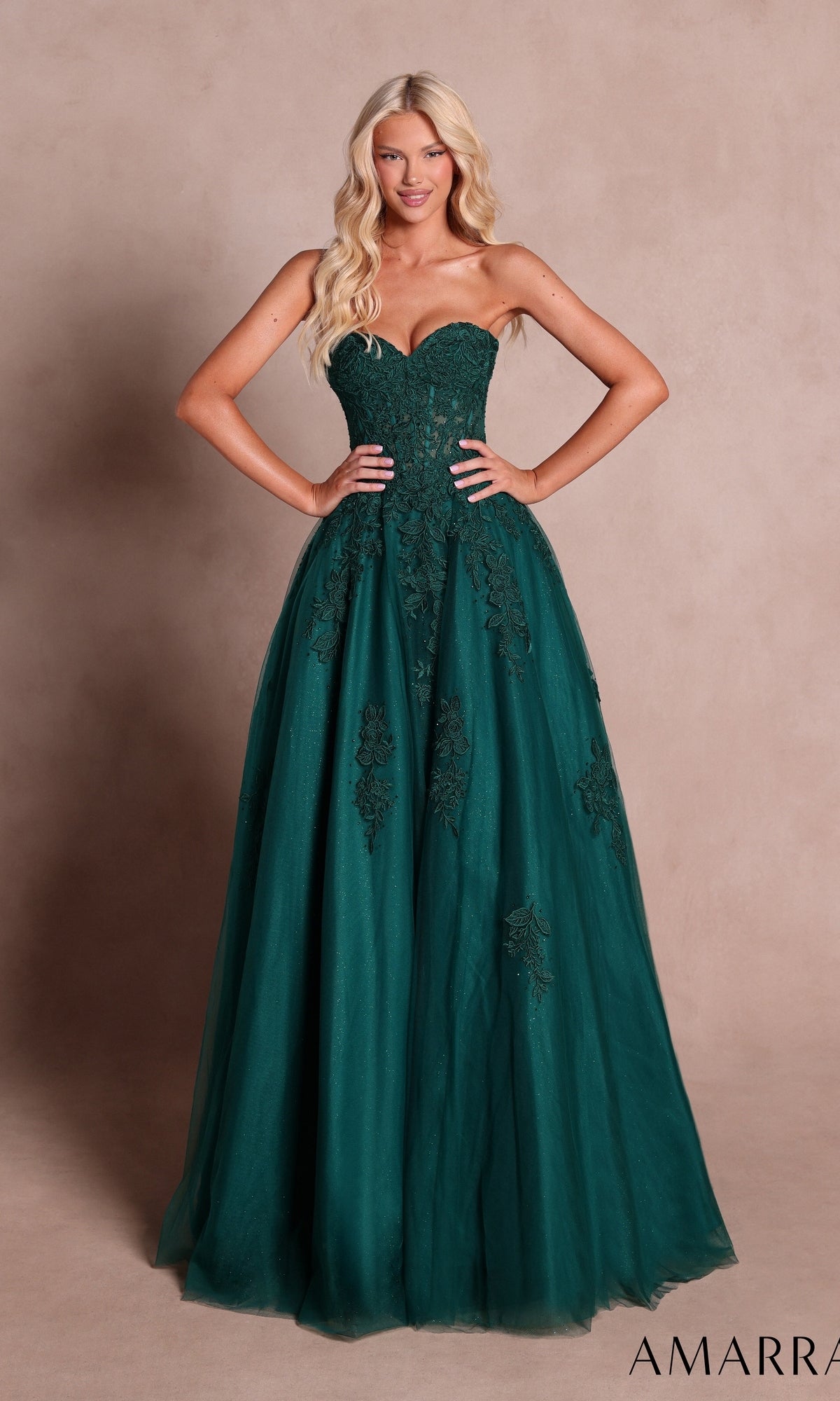 Model showcases the Amarra 89688 Long Prom Dress in emerald, a strapless, floor-length gown featuring lace appliqué details and a flowing ball-gown skirt, set against a plain beige background.