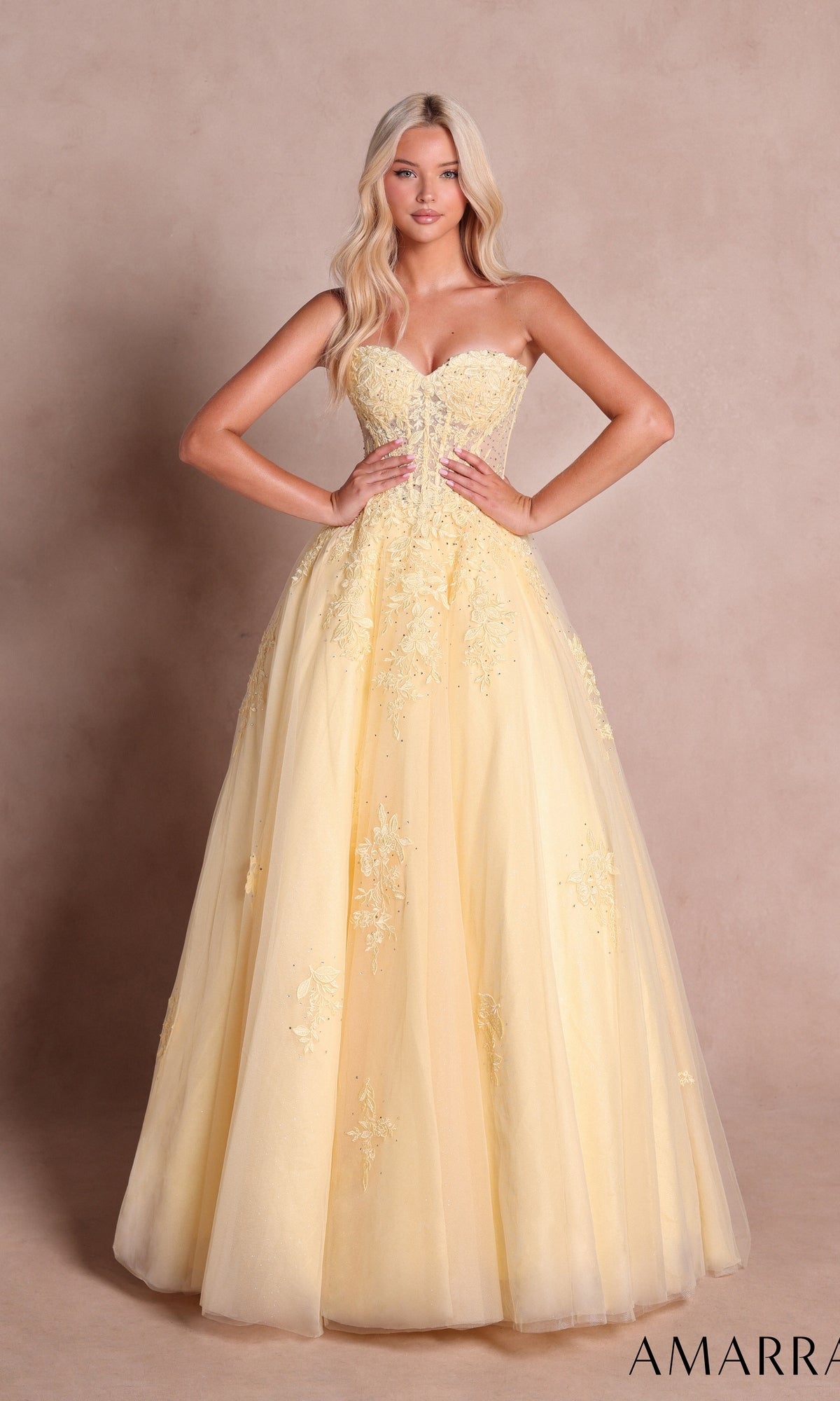 A woman wearing the Amarra 89688 long prom dress in light yellow, featuring a strapless design, floral embroidery, and a classic floor-length ball-gown skirt, stands against a neutral background.