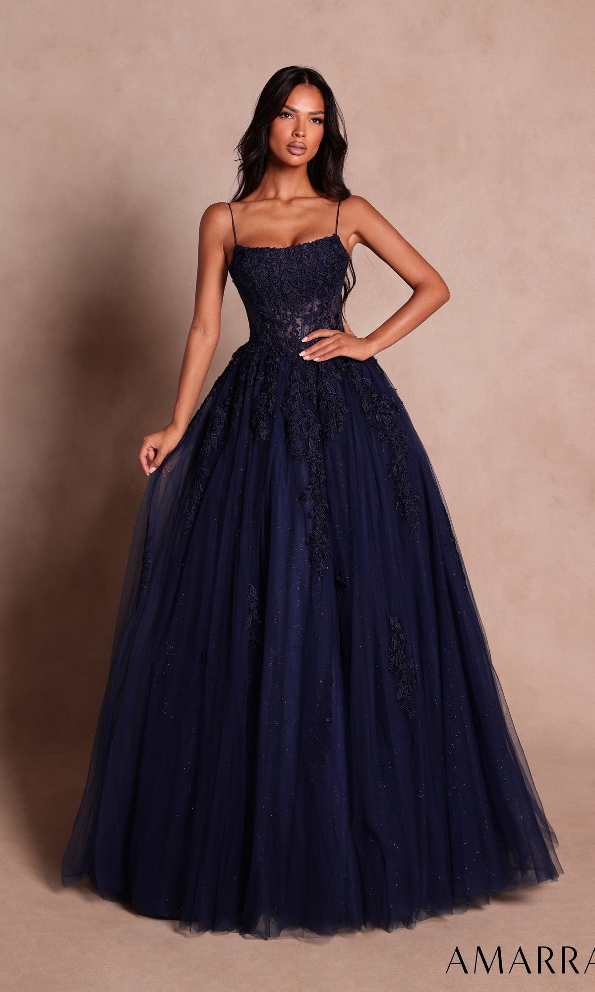 A woman wearing the Amarra 89806 Long Prom Dress in navy, a floor-length gown featuring floral lace and tulle details, stands against a neutral background.