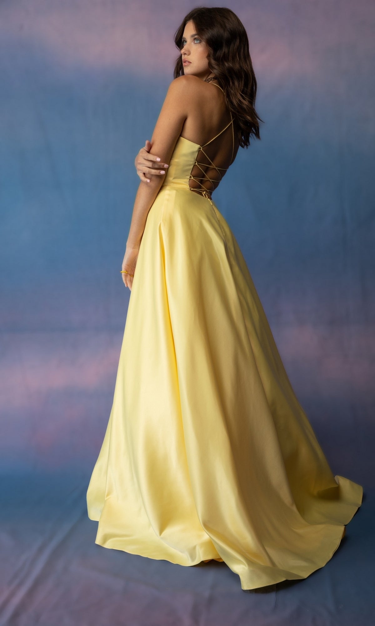 A person wearing a yellow Eureka 9008 Strappy-Back Long Satin Prom Dress featuring a long, satin formal design with a strappy open-back and lace-up detail.