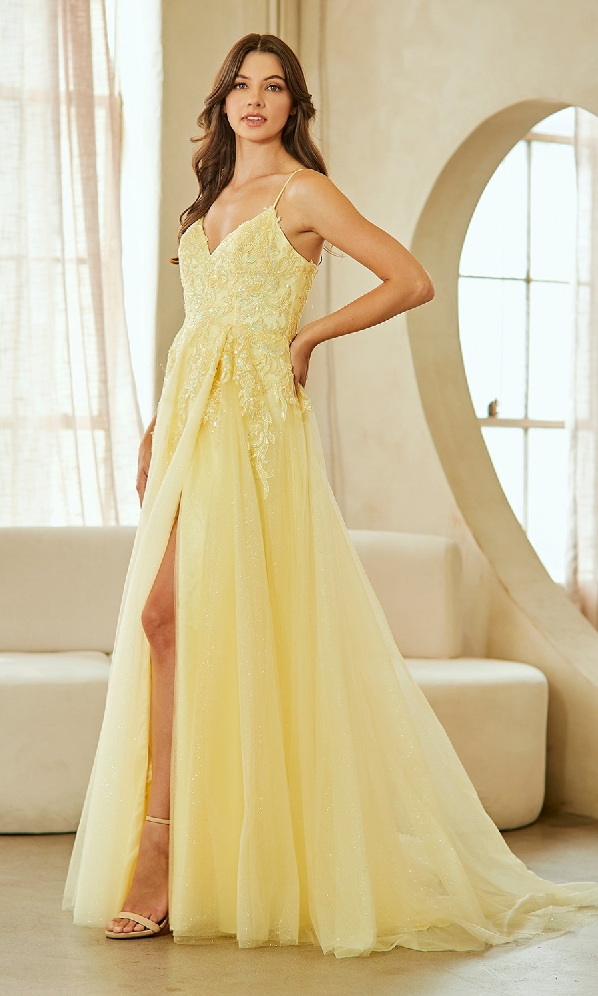 Woman wearing a yellow evening gown with a high slit in a well-lit room.