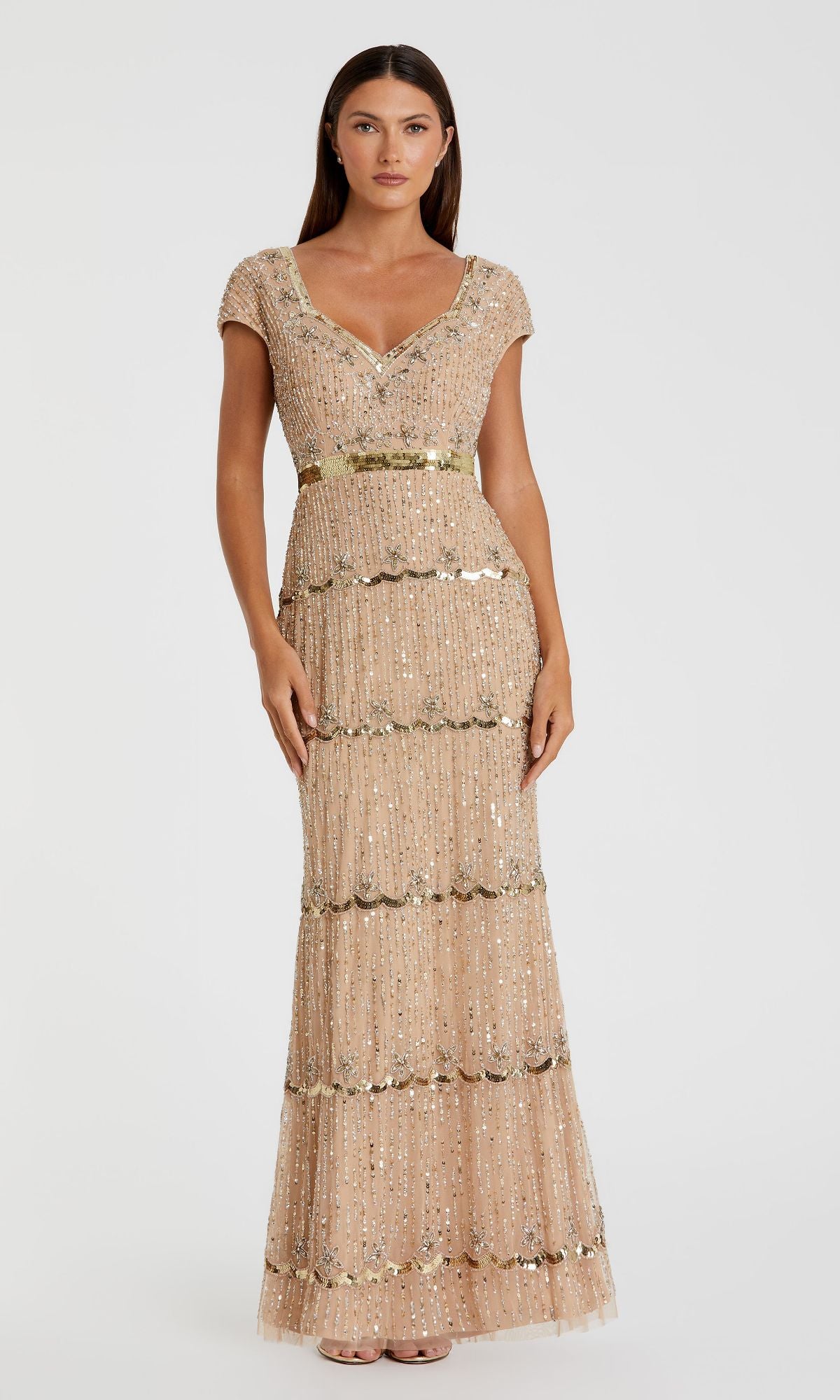 A woman wears the Mac Duggal 9089 Cap-Sleeve Beaded Formal Dress, a floor-length beige gown with gold sequin embellishments and scalloped details, standing against a plain white background.