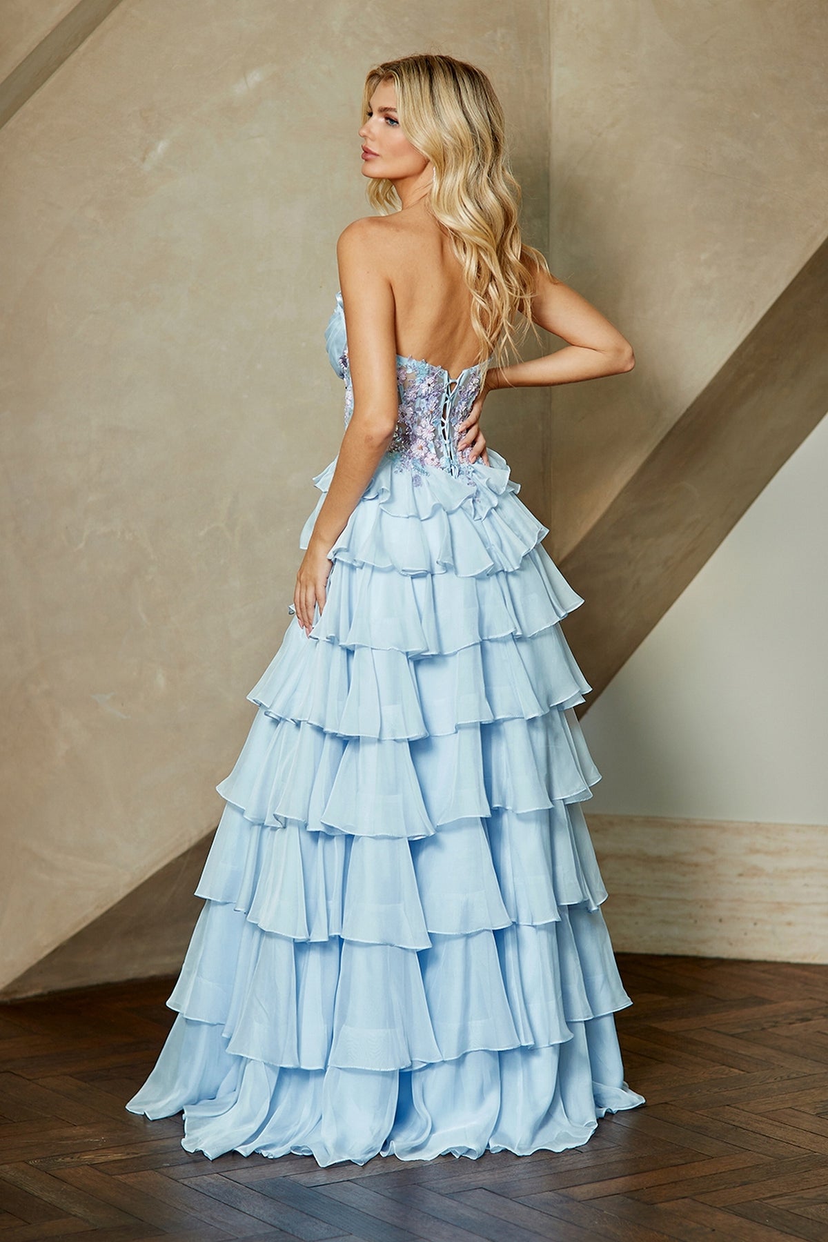 A woman wearing the Long Prom Dress: Amelia Couture 9103, a light blue, strapless gown with a beaded corset bodice and a tiered, ruffled chiffon skirt.