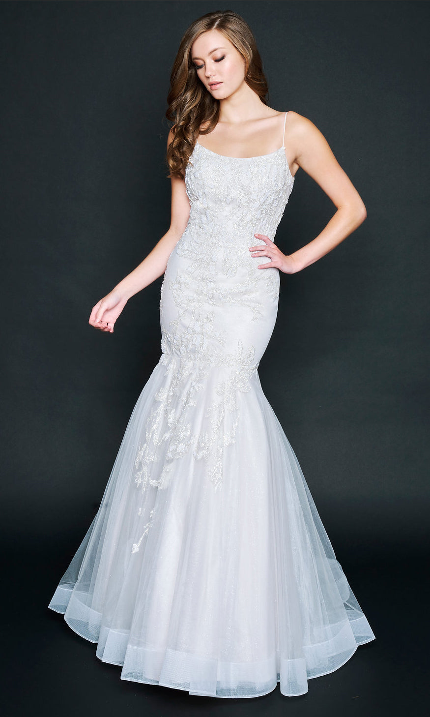 Woman wearing the Nina Canacci 9120 long formal dress, a sleeveless white mermaid gown with elegant lace details, stands against a plain dark background.