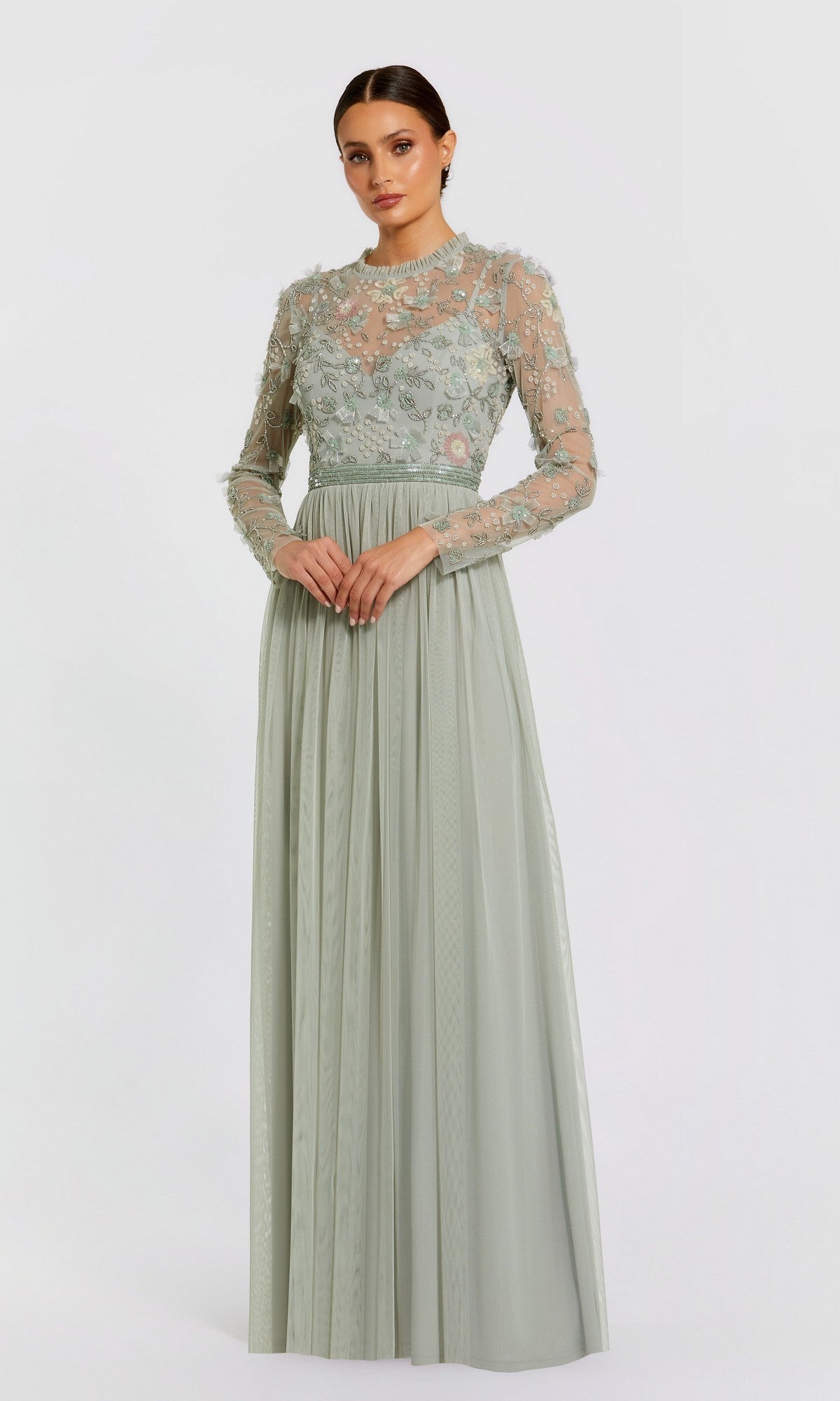 Woman in the Mac Duggal 9132 Long Sleeve Vanilla Formal Gown with sheer, embroidered sleeves and a fitted waistband, standing against a plain background.