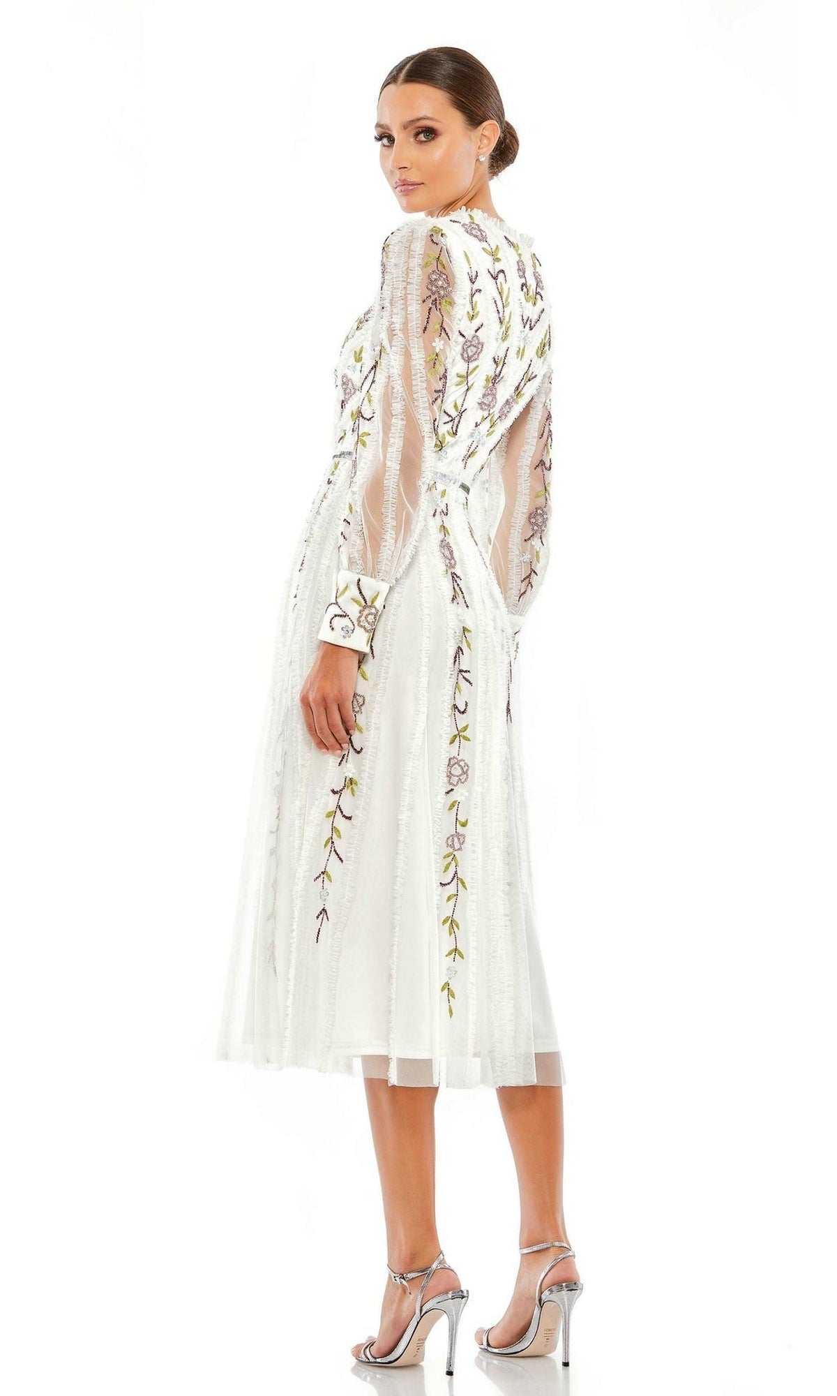 A woman models the Mac Duggal Knee Length Wedding Guest Dress 9133 featuring sheer embroidered sleeves and floral patterns, styled with silver heels—perfect for a semi-formal occasion.