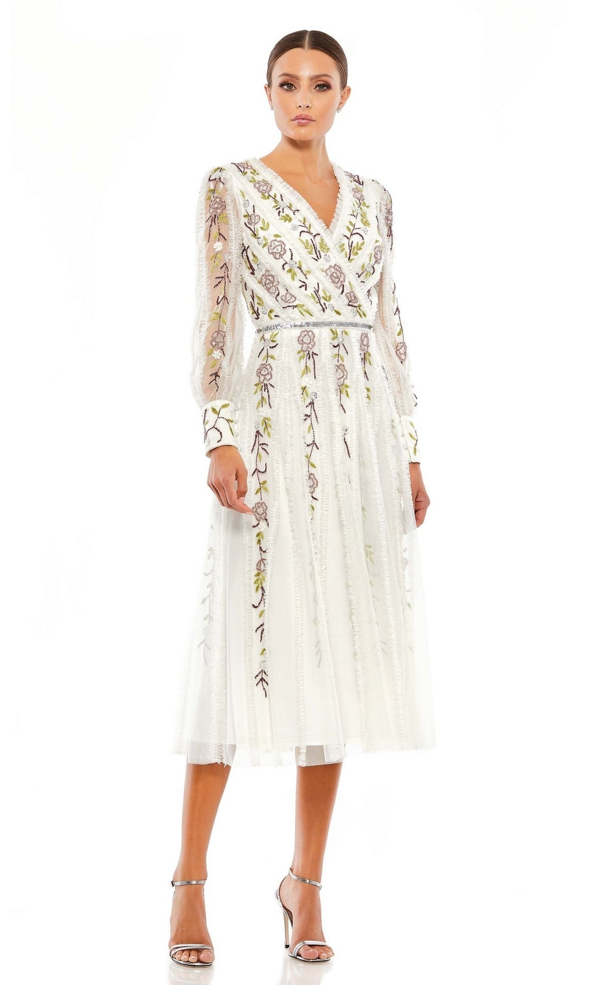 A woman wears the Knee Length Wedding Guest Dress 9133 by Mac Duggal, featuring white long sleeves and floral embroidery, paired with silver high heel sandals against a white background.