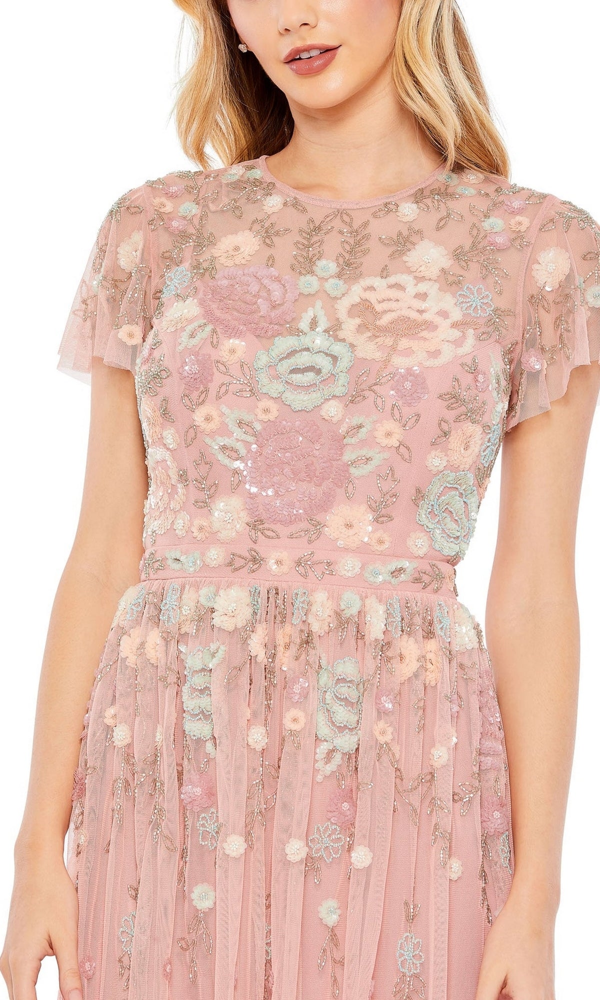 A woman wears the Mac Duggal Knee Length Wedding Guest Dress 9134, a short-sleeved blush pink floral design with embroidery and sequin details. The elegant dress is shown in a cropped image from below the shoulders to above the knees.