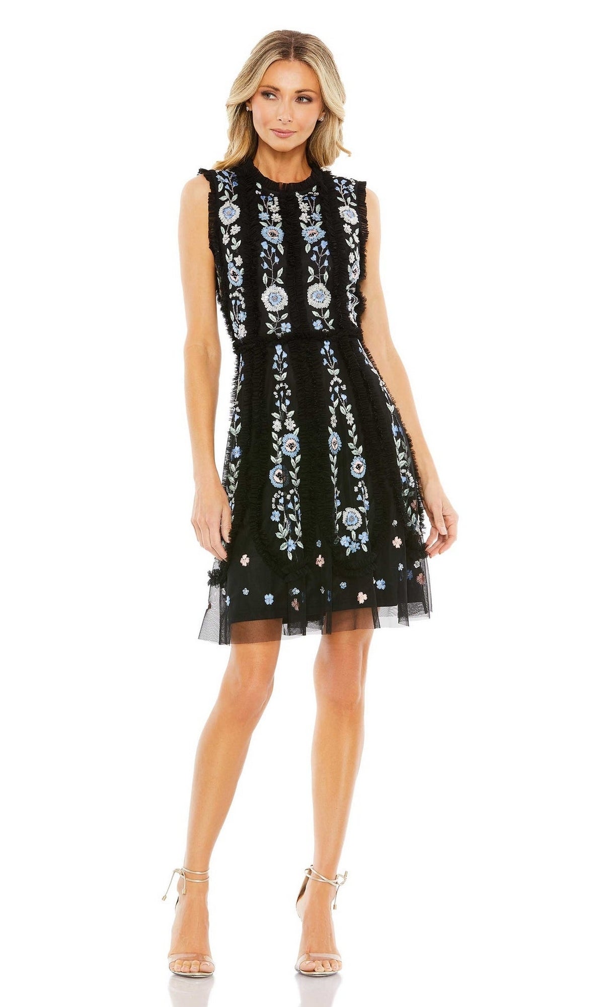 A woman models the Mac Duggal 9135 embroidered short party dress with blue and white floral accents, sleeveless and black, paired with neutral heels against a plain white background.