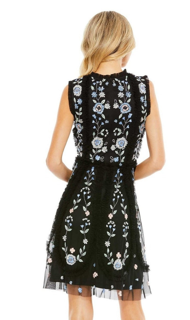A blonde woman wears the Embroidered Short Party Dress: Mac Duggal 9135—a sleeveless black cocktail dress with blue and white floral embroidery—shown from the back.