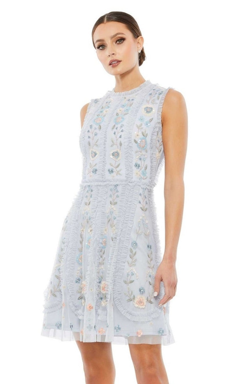 Woman in a sleeveless, light blue Mac Duggal 9135 Embroidered Short Party Dress with floral embroidery and ruffle details, standing against a white background.