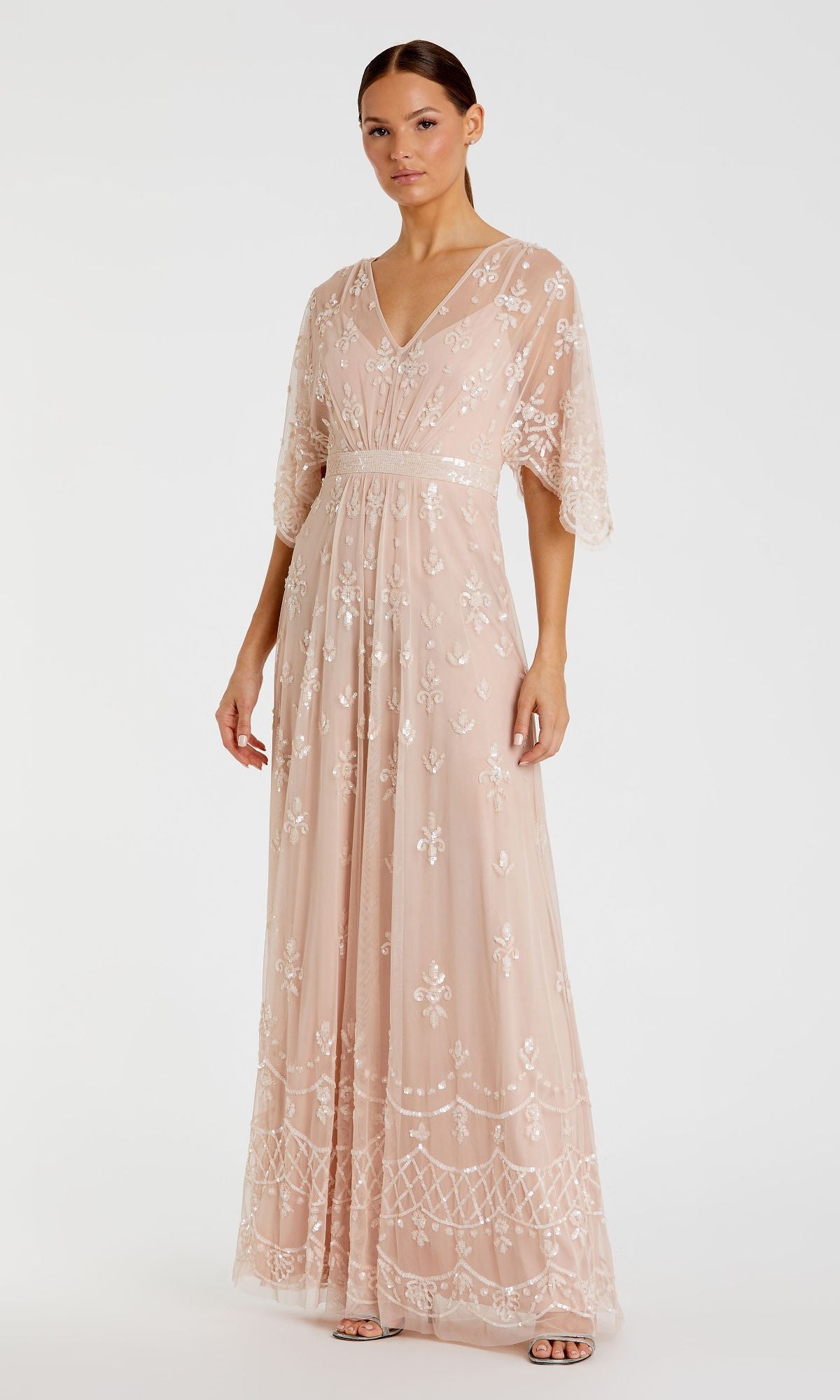 A woman poses against a white background in the Mac Duggal 9144 Long Pink Sequin Formal Dress, featuring semi-sheer fabric, white floral embroidery, short flutter sleeves, and a V-neckline.