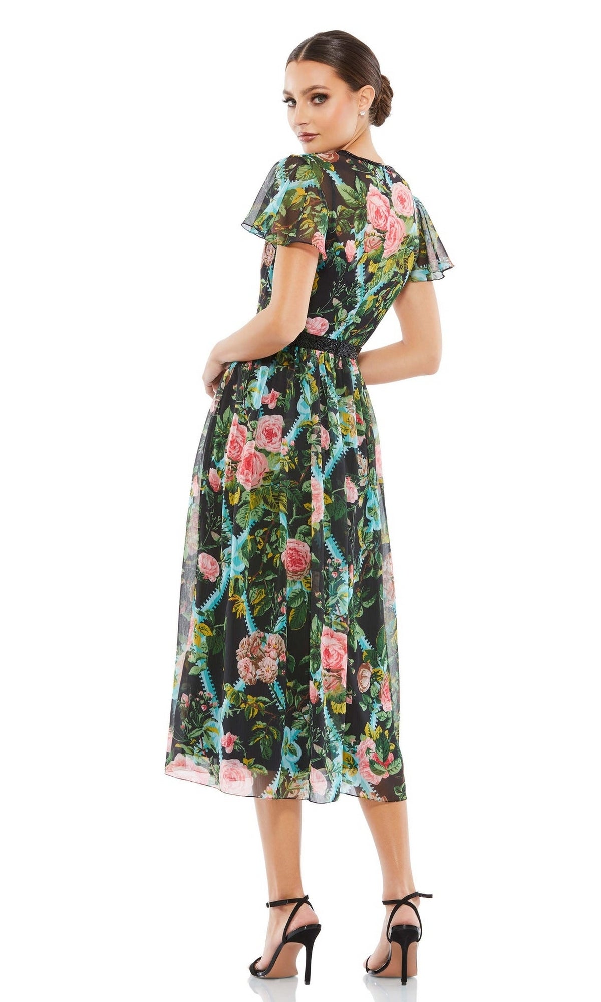 A woman stands looking over her shoulder, wearing the Mac Duggal 9149 Print Midi Wedding-Guest Dress with short sleeves and black high-heeled sandals.
