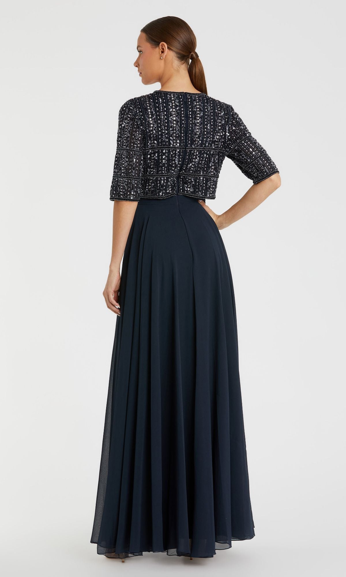 A woman faces away from the camera in the Mac Duggal 9180 short sleeve long formal dress, featuring a navy blue A-line silhouette with a beaded bolero jacket.