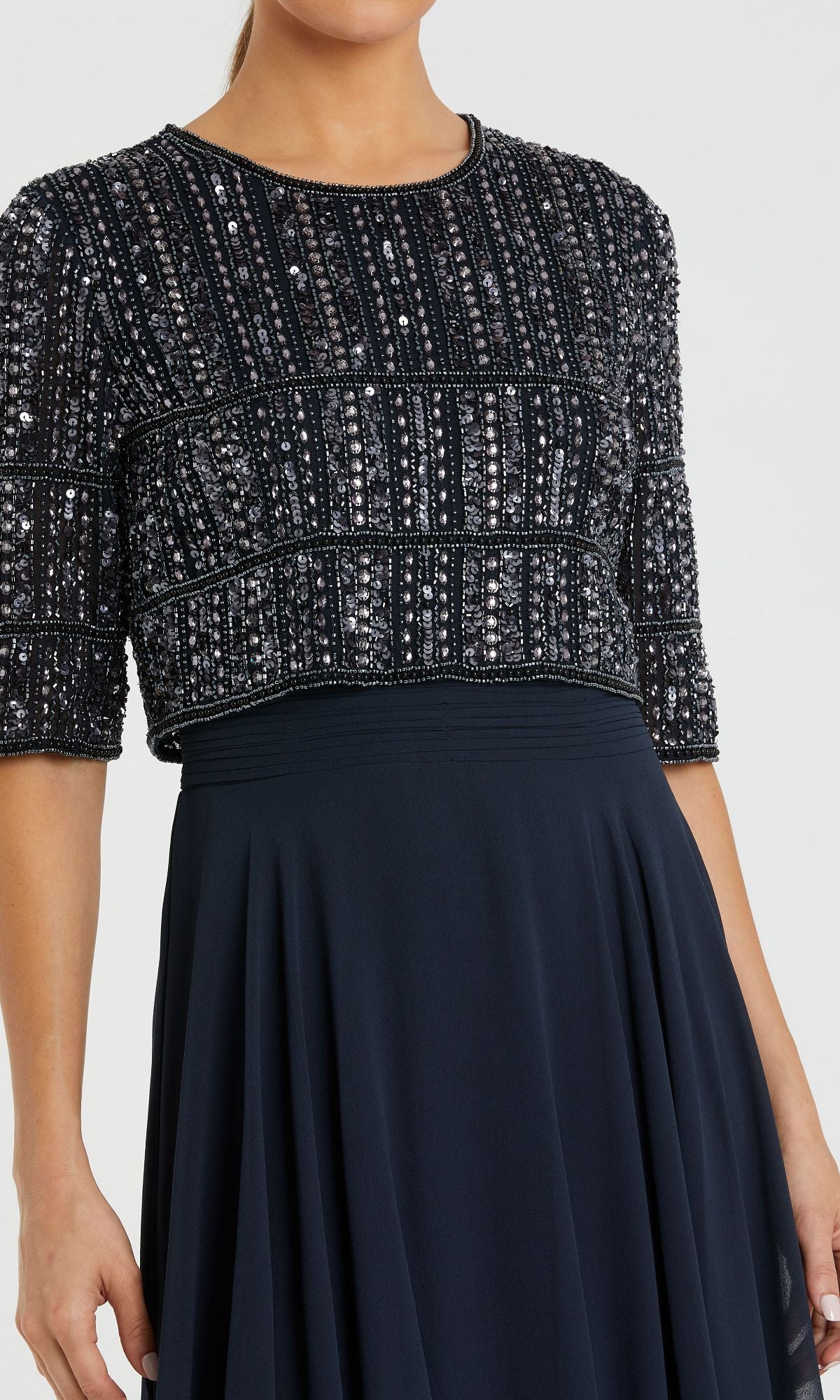 A woman wears the Mac Duggal 9180, a navy long formal dress with short sleeves, a fitted beaded bodice, and a plain flowing A-line skirt.
