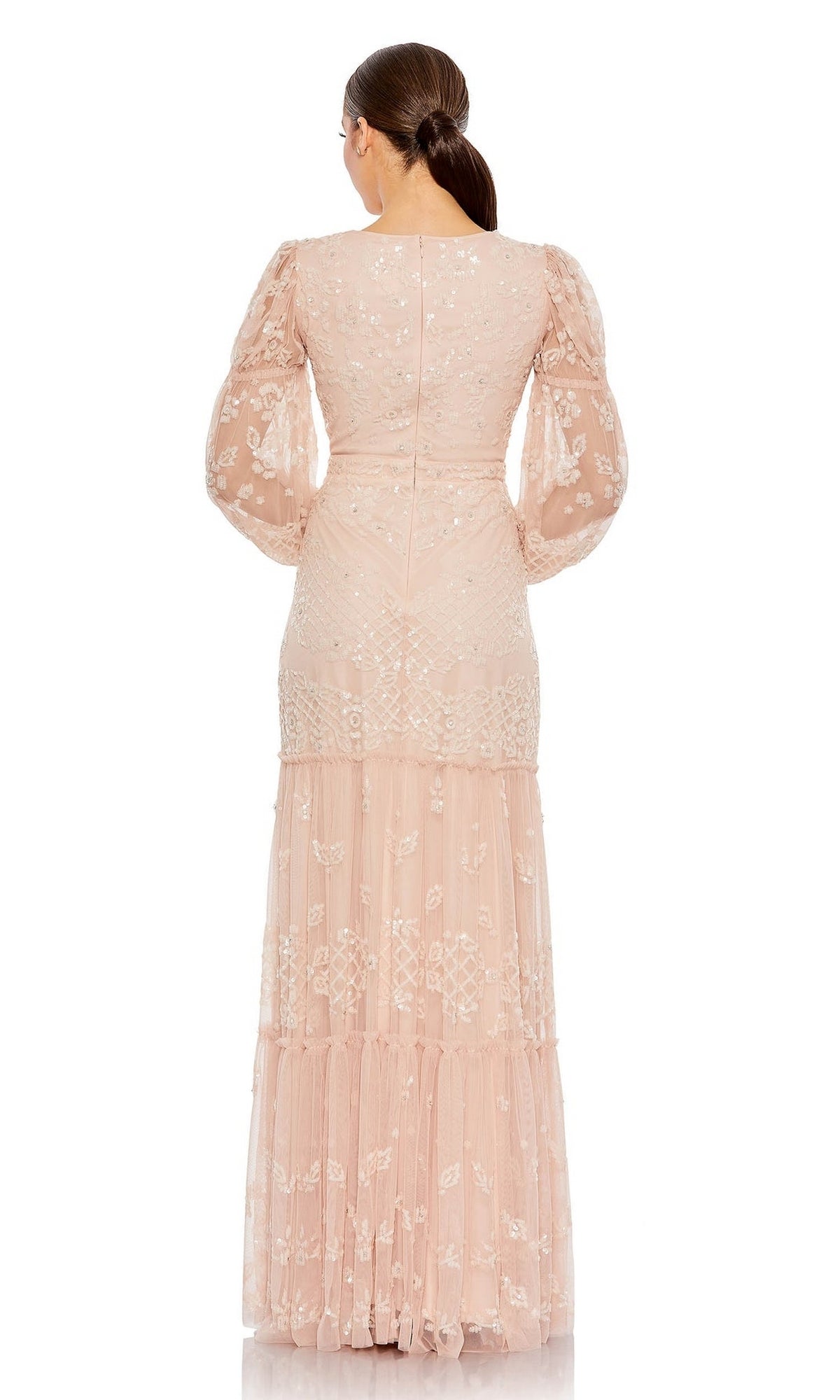 A woman faces away in the Long Formal Dress 9197 by Mac Duggal—a blush pink, floor-length gown with lace details, puffed sheer sleeves, and a tiered skirt. Her hair is styled in a low ponytail against a plain white background.