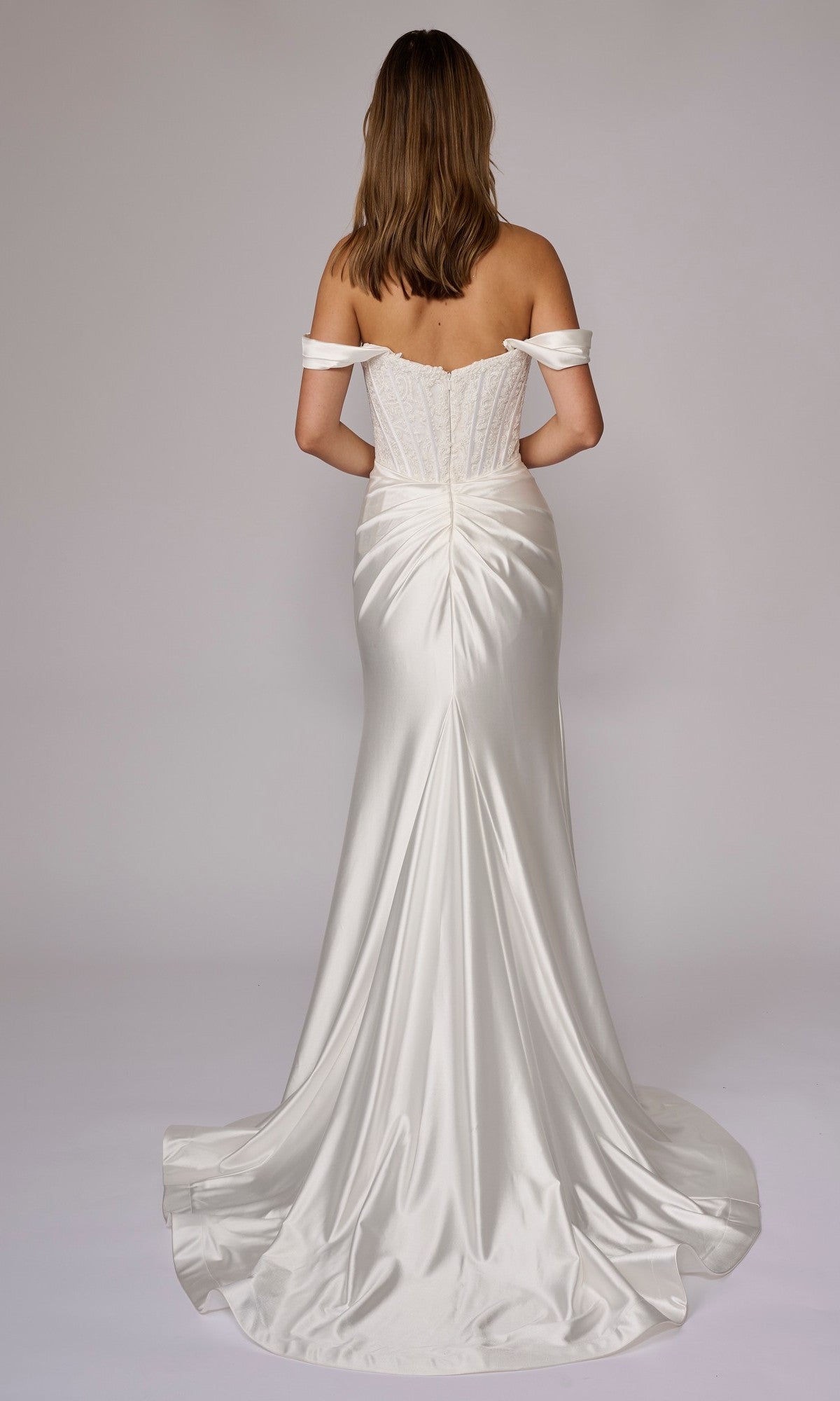 A woman models the Nina Canacci 9202 long formal dress, featuring an off-the-shoulder embellished corset bodice and satin skirt, shown from the back against a plain light background.