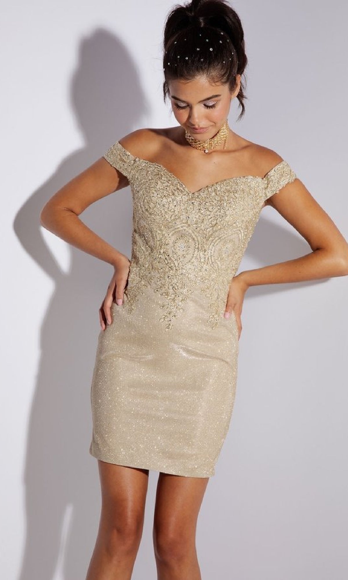 A woman models the Short Glitter Wedding-Guest Dress: Eureka 9206—an off-the-shoulder, gold, fitted dress with intricate embroidery and a shimmering finish—against a plain background, perfect for any cocktail party.