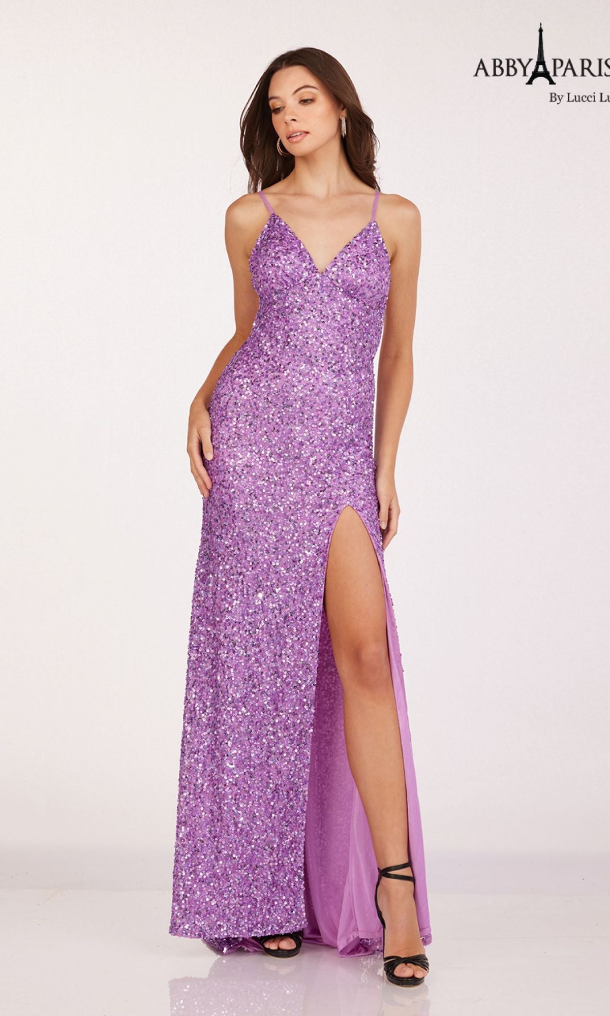 A woman stands against a plain light background wearing the Abby Paris 92113 Backless Fitted Sequin Prom Dress in sparkling lavender, featuring a v-neck and thigh-high slit.