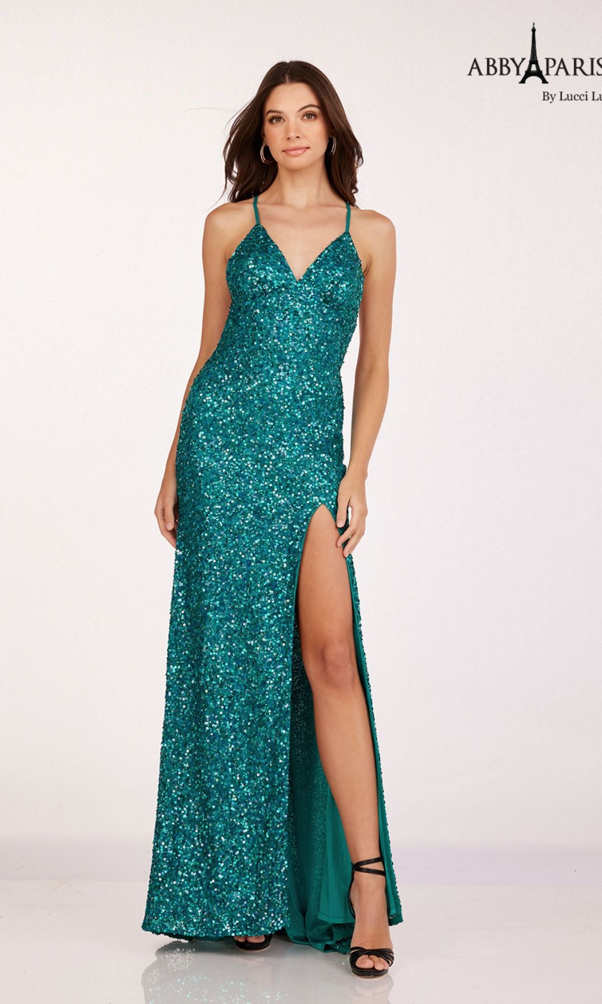 A woman wearing the Abby Paris 92113 Backless Fitted Sequin Prom Dress in teal, featuring spaghetti straps, a v-neckline, and a high slit, stands against a plain light background.