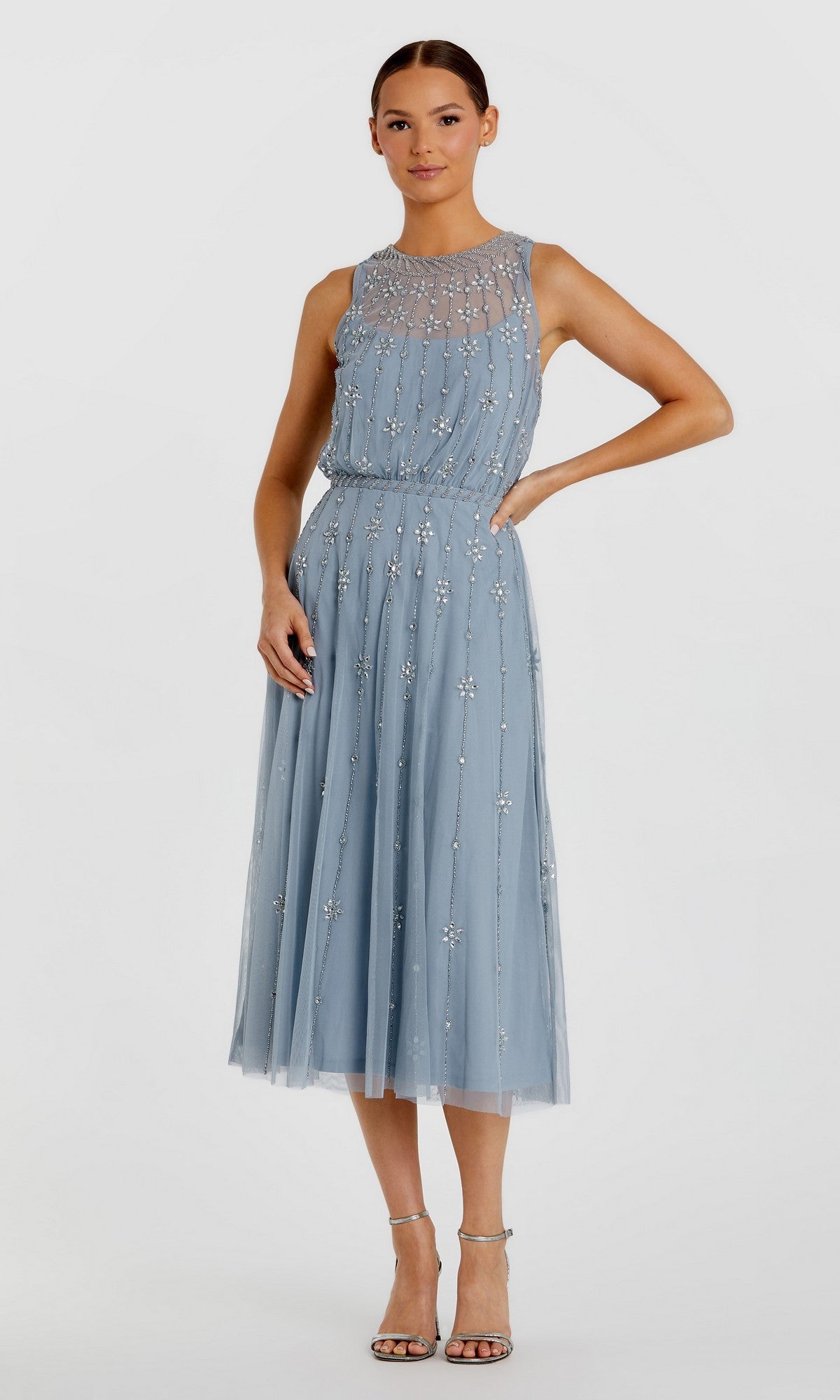 A woman wears the Mac Duggal 9222 Midi Wedding Guest Dress in powder blue, sleeveless with beaded detailing, paired with silver high-heeled sandals, standing against a plain white background.