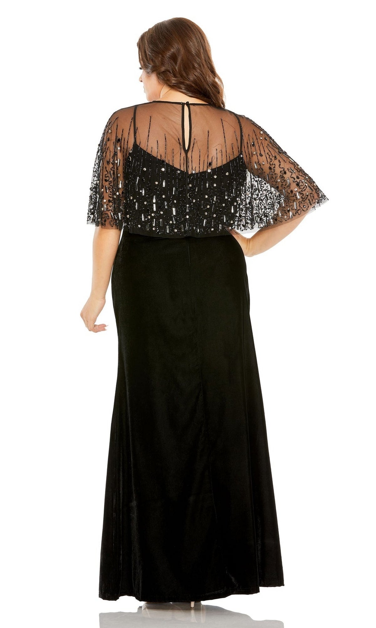 A woman stands facing away from the camera in the Mac Duggal 9228 long plus-size formal dress, featuring black velvet, a v-neckline, and an embellished sheer cape.