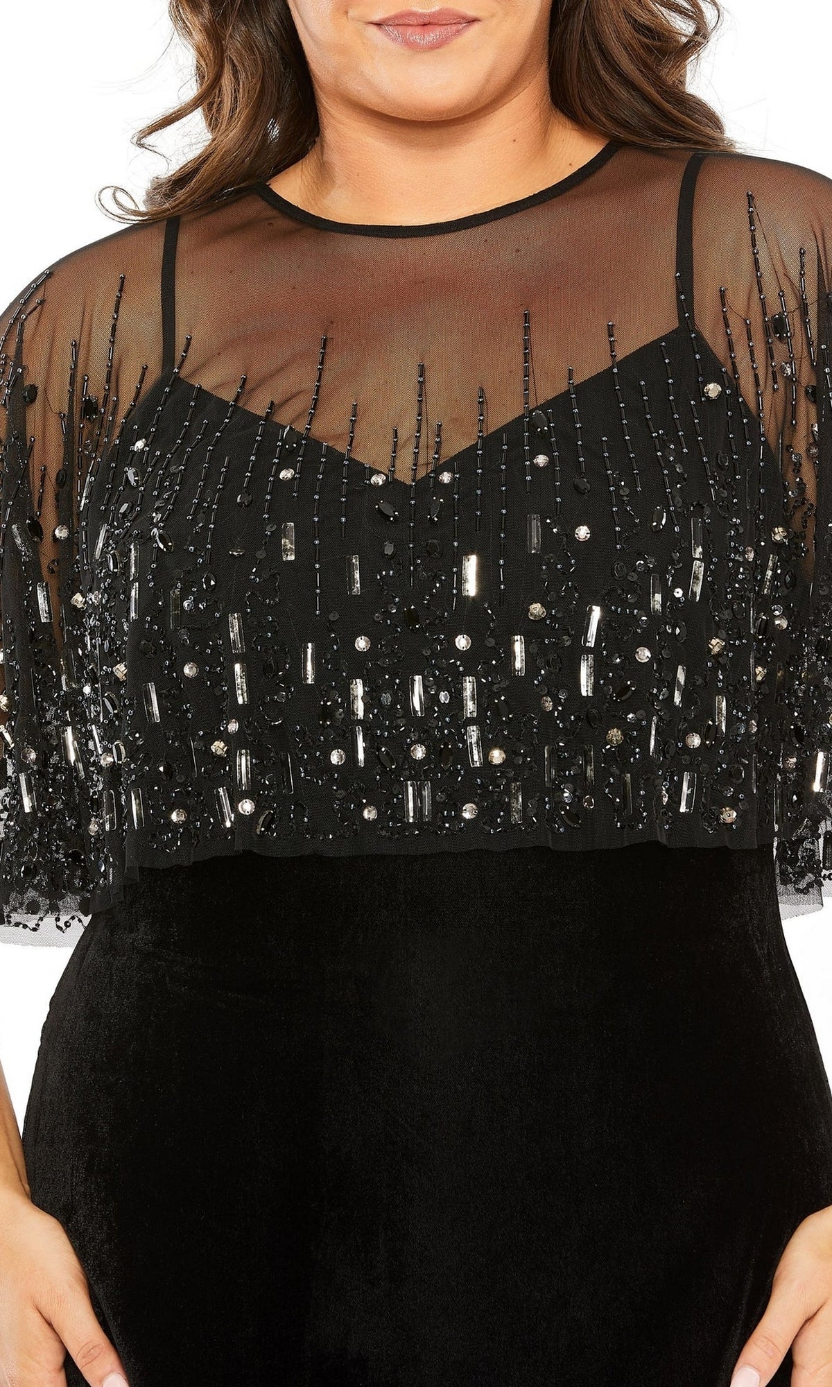 A woman wearing the Mac Duggal 9228 Long Plus-Size Formal Dress—a black gown with a v-neckline, sheer beaded overlay, and sequin-embellished bodice.